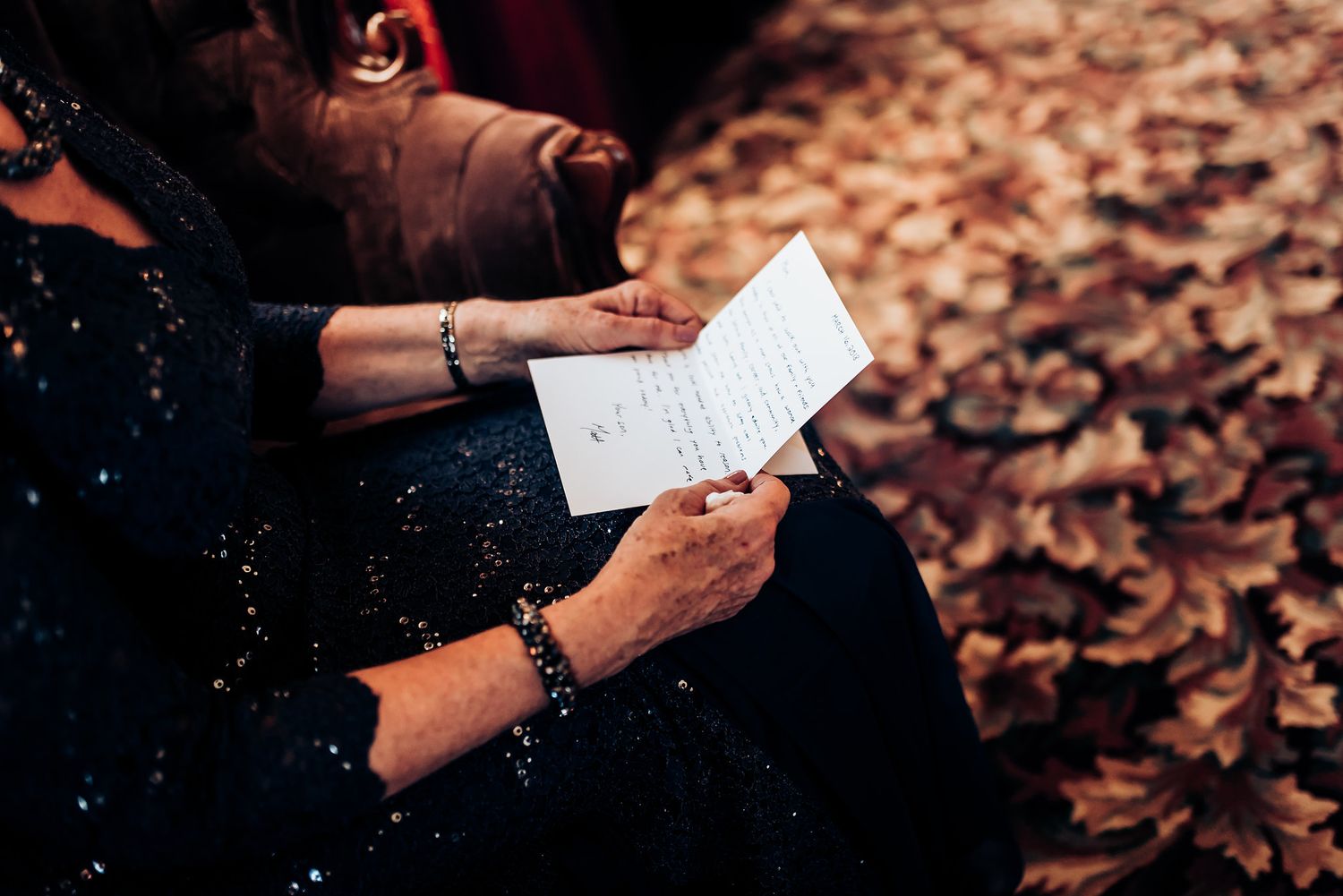 Hands hold a handwritten note against a background of fallen autumn leaves.