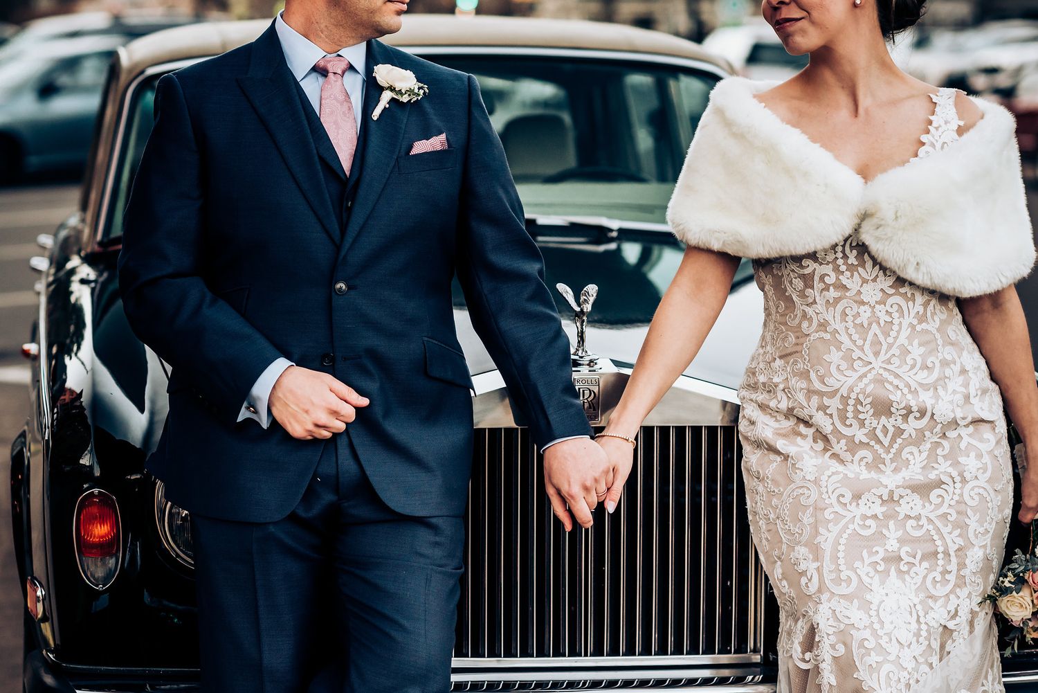 Wedding couple poses beside luxury Rolls Royce in formal attire.