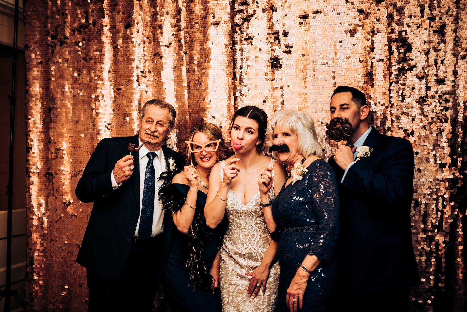 Party guests pose together against a rose gold sequin backdrop at a formal event.
