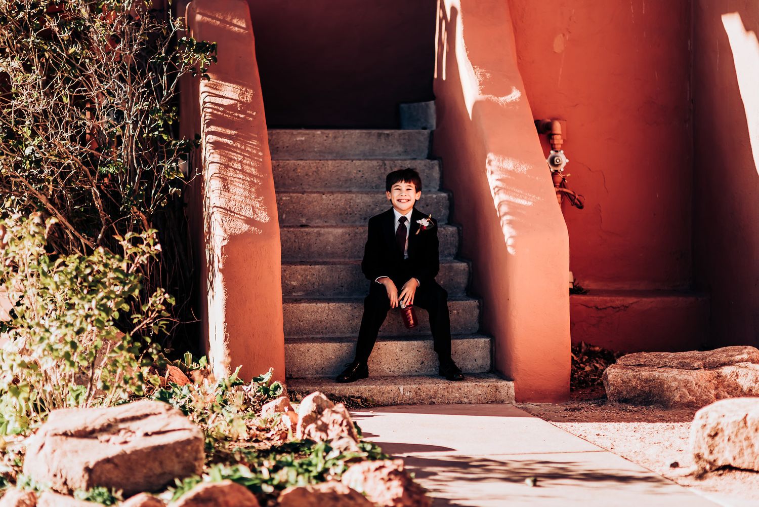 A solitary figure sits on red painted stairs in formal attire.