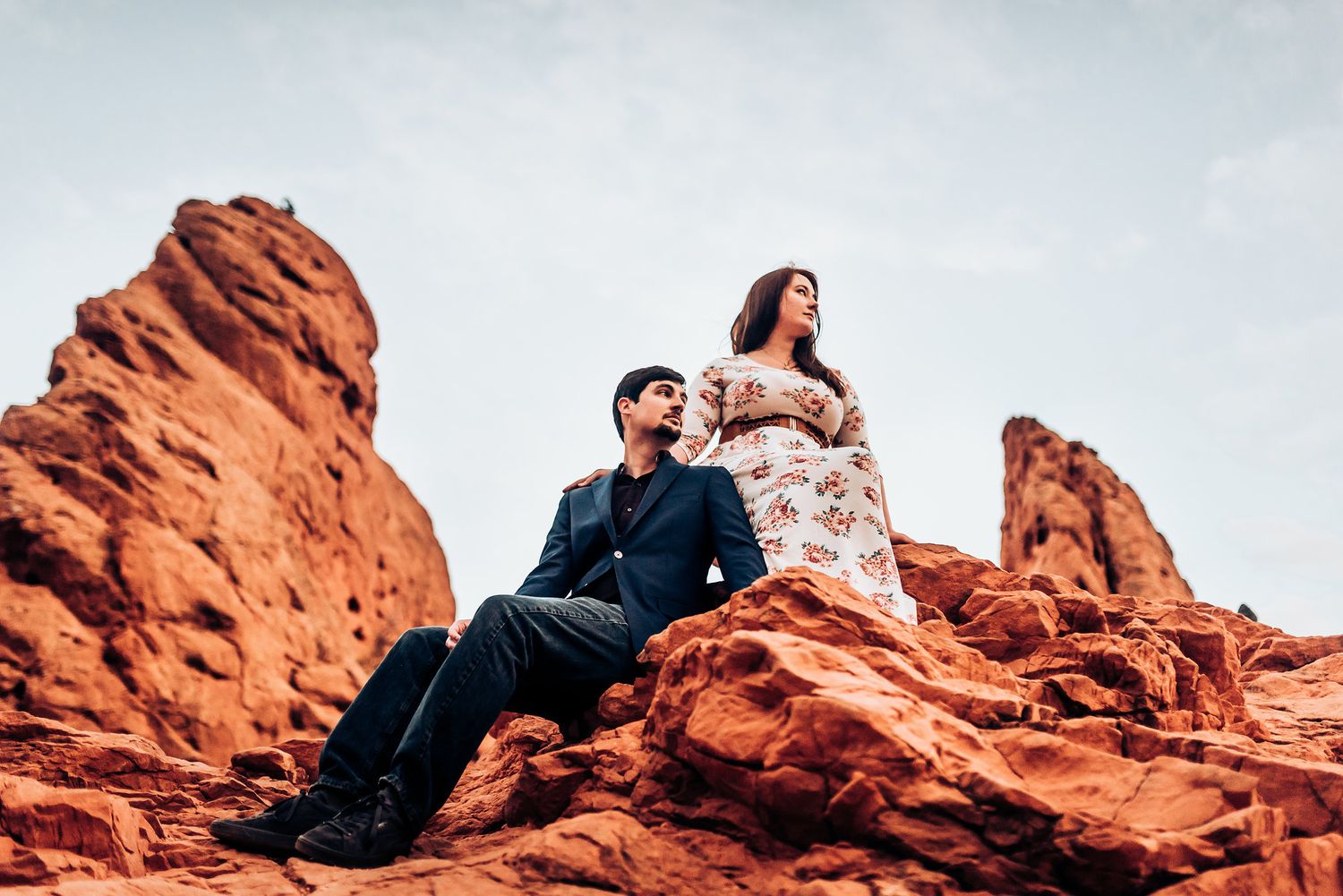 Couple poses on red rock formations with mountains in background during engagement photoshoot.