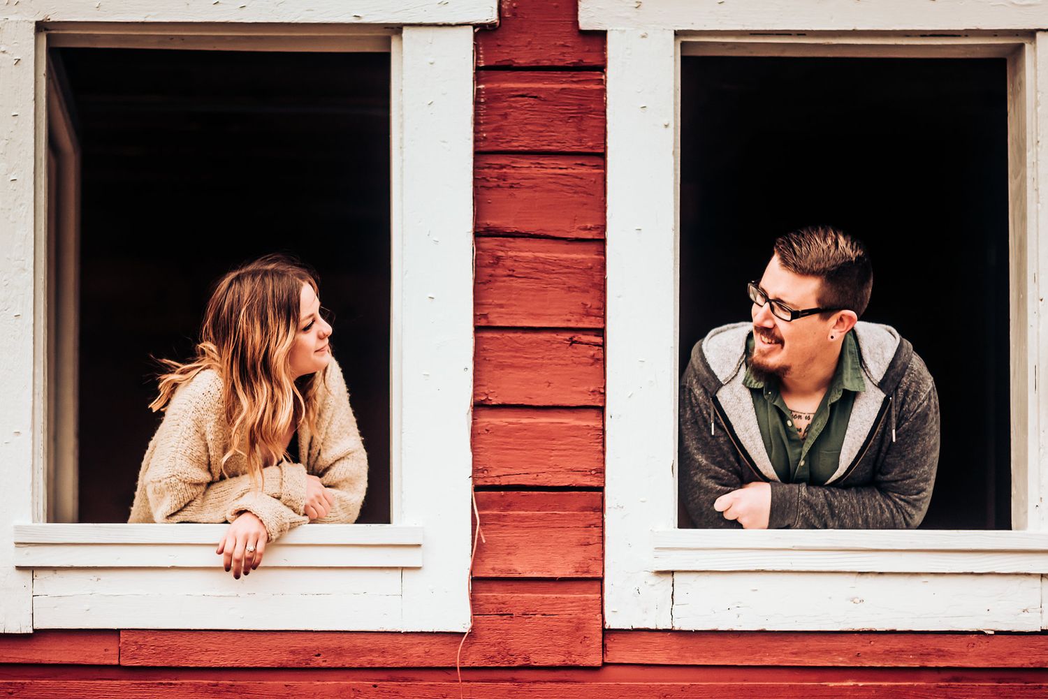 A playful couple leans out separate windows of a red building.