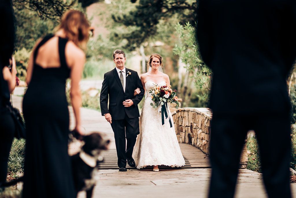 Wedding ceremony processional on a stone path surrounded by trees and greenery.