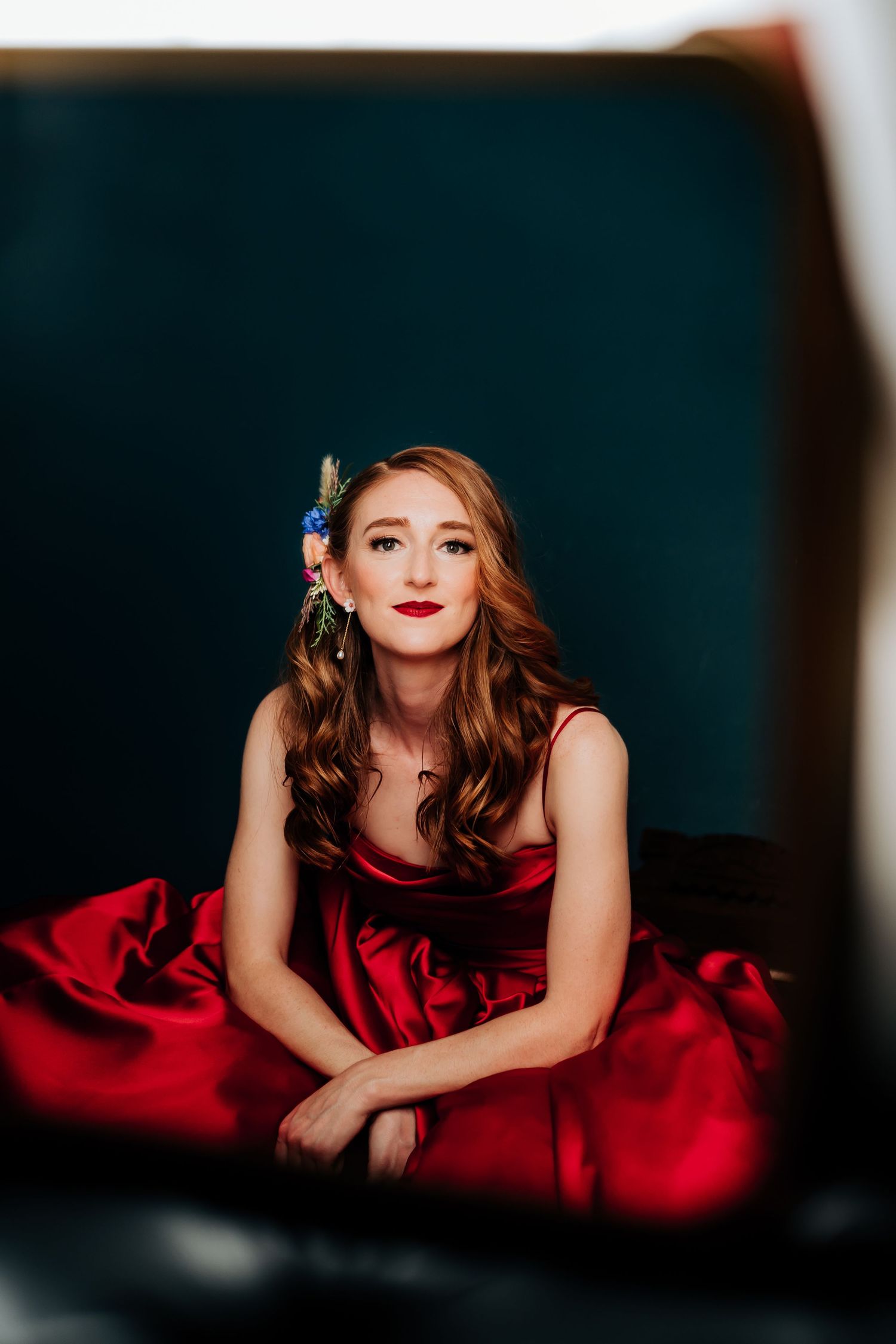 Glamour portrait of someone in red dress lying down against dark background.