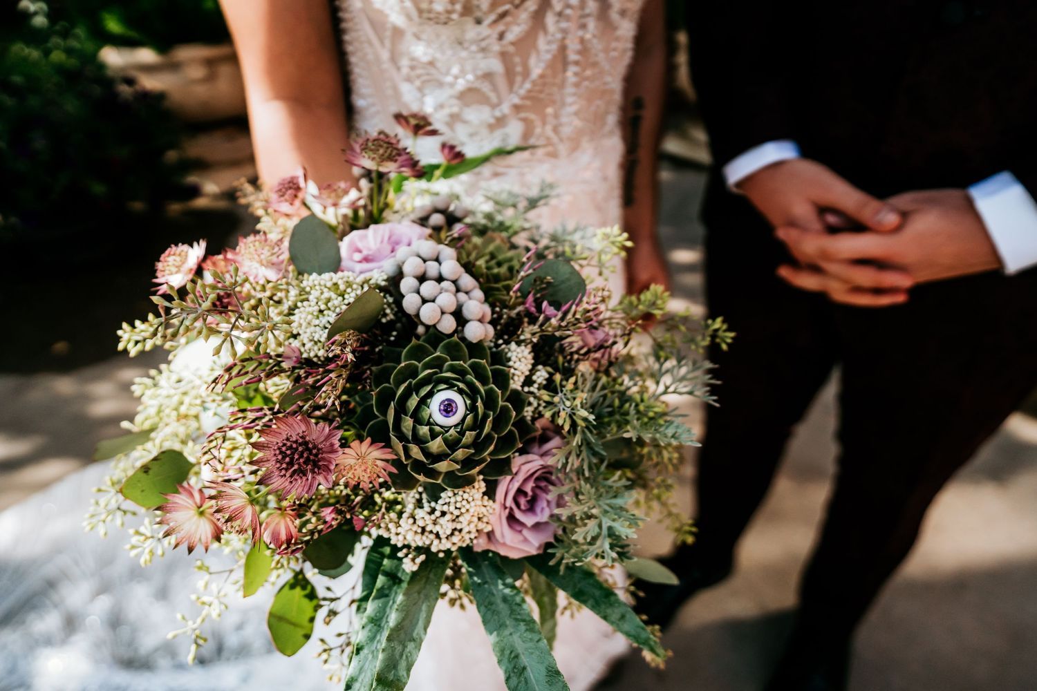 Delicate wedding bouquet with pink roses and greenery against dark background.