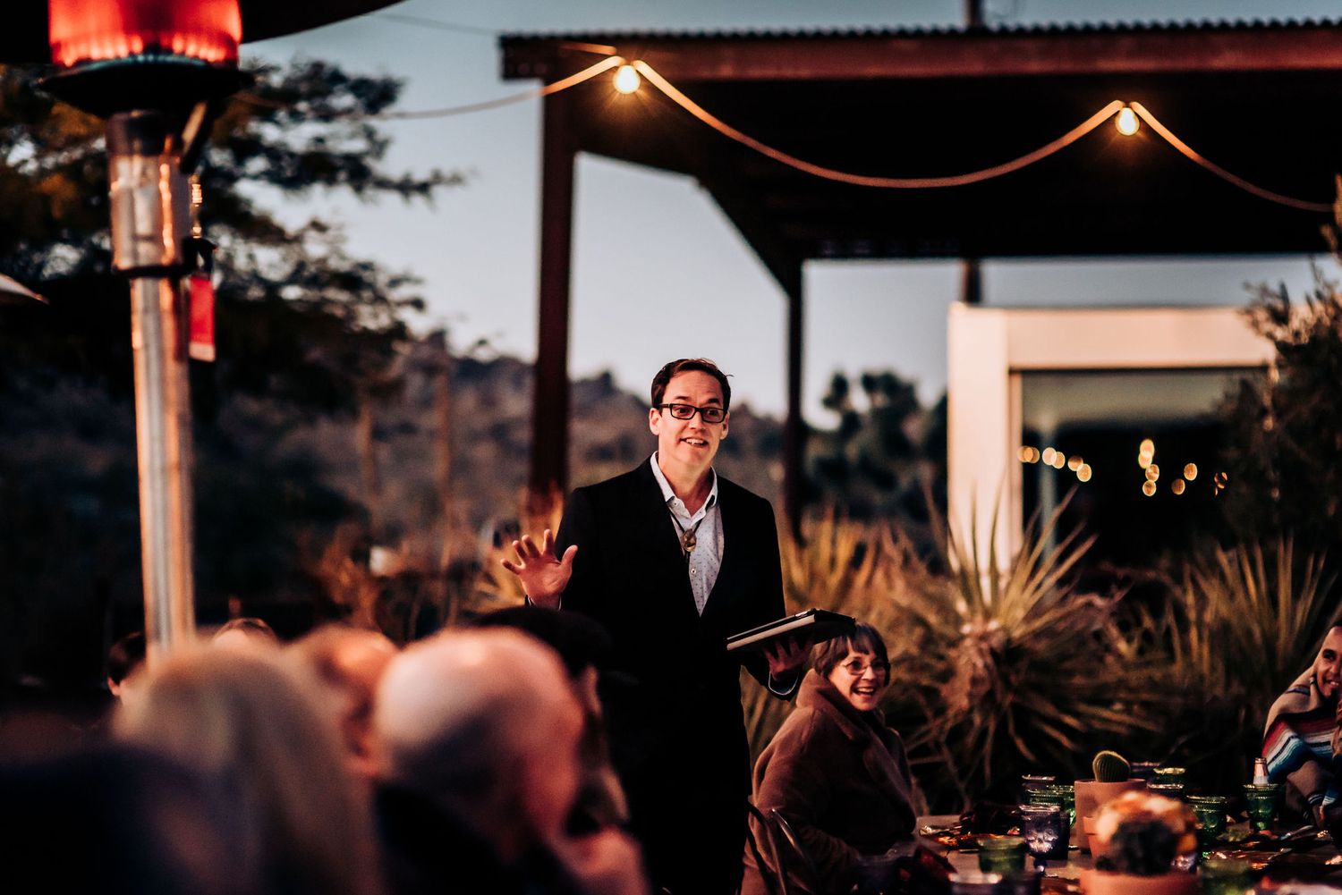 Evening outdoor event with string lights and desert scenery in background.