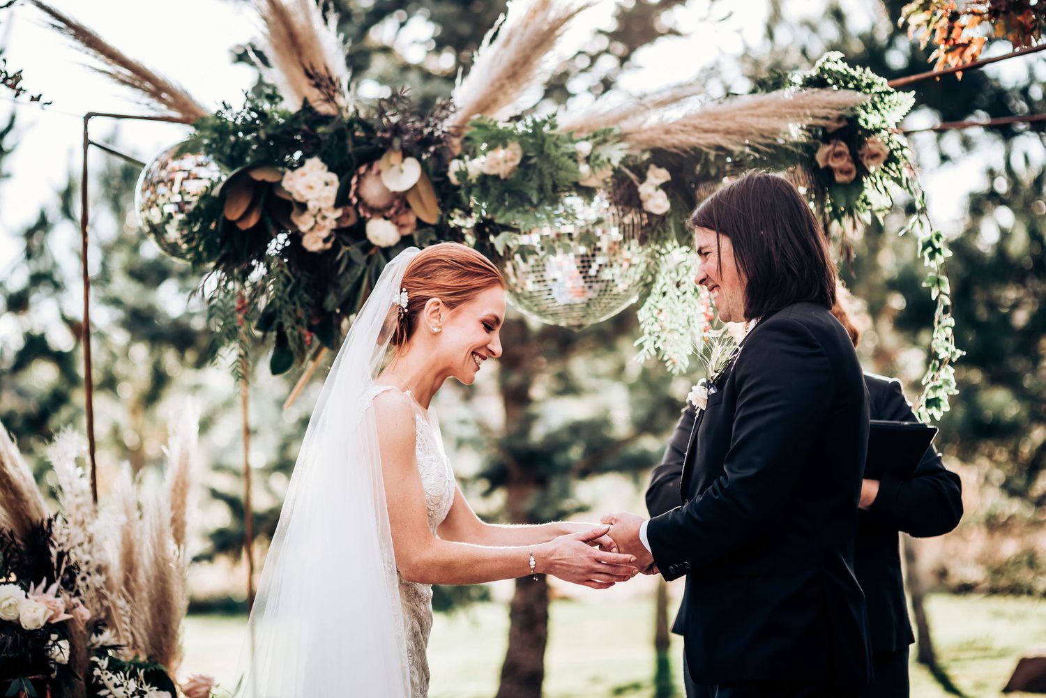 Romantic wedding ceremony moment under rustic floral arch with dried pampas grass.