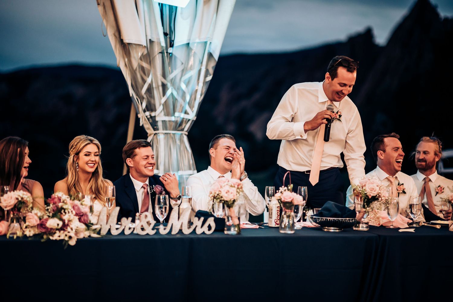 Wedding party seated at head table during evening reception toasts.