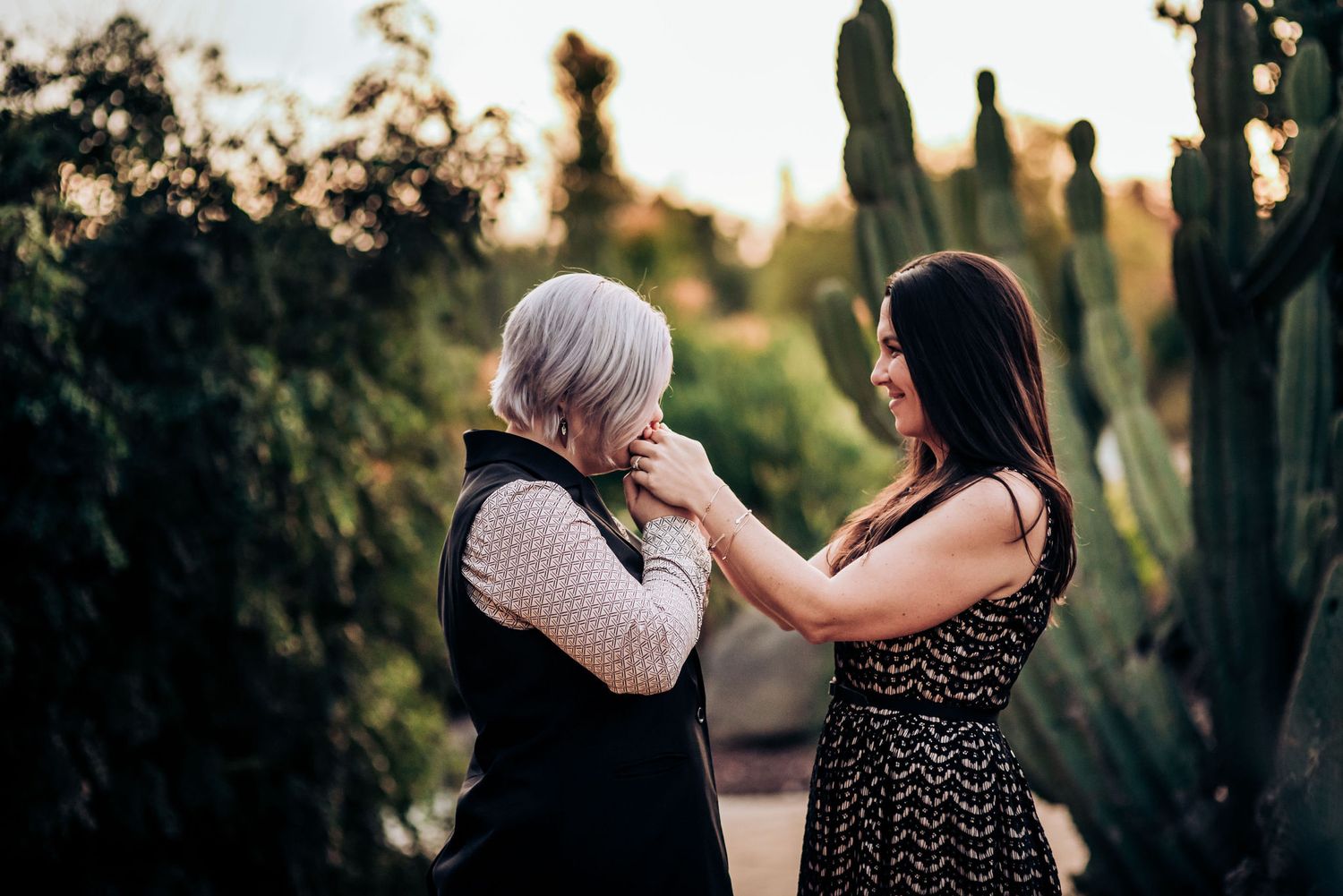 Two people share a tender moment while standing on a path surrounded by desert plants.