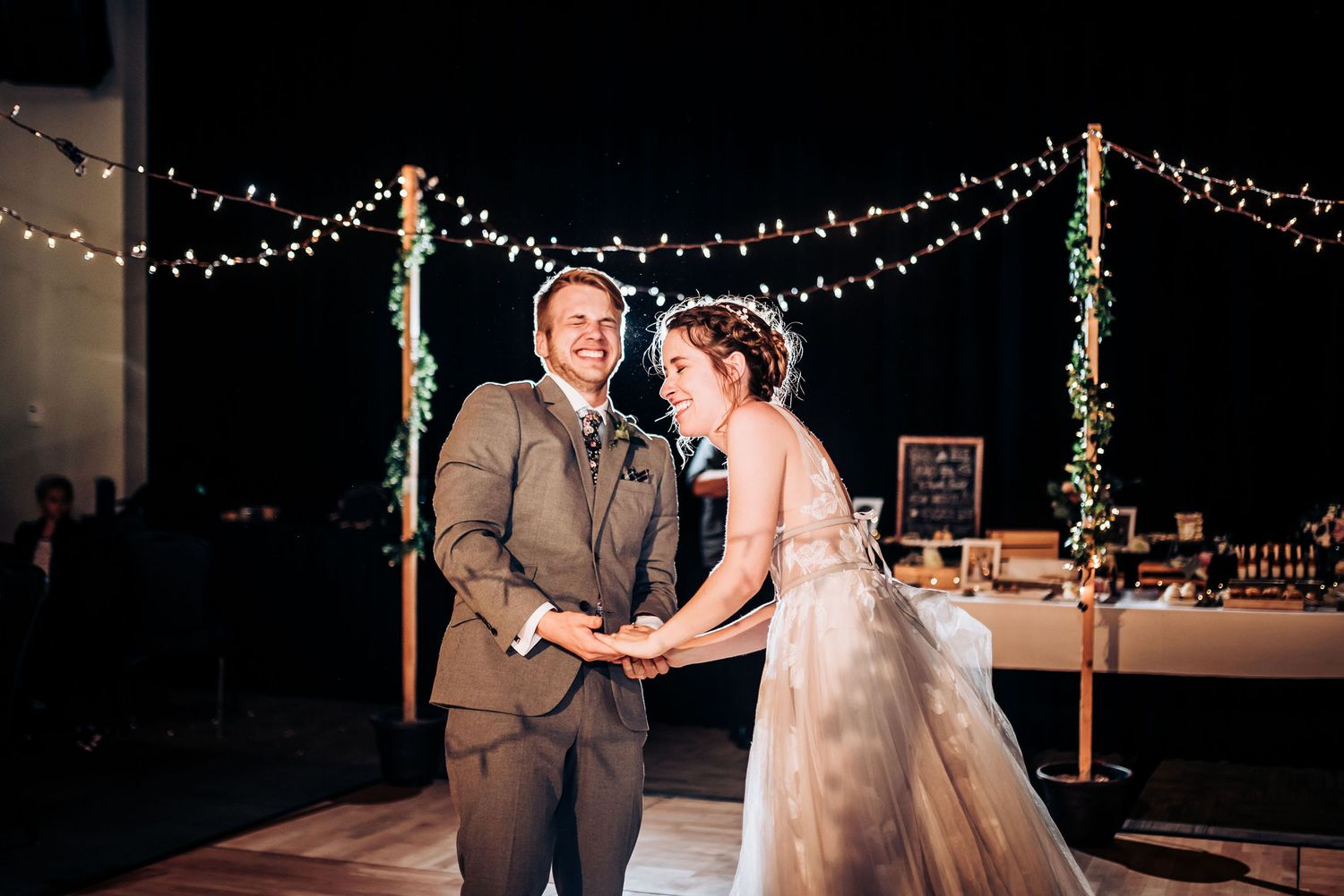 A couple shares an intimate moment during their wedding dance under string lights and decorated poles.