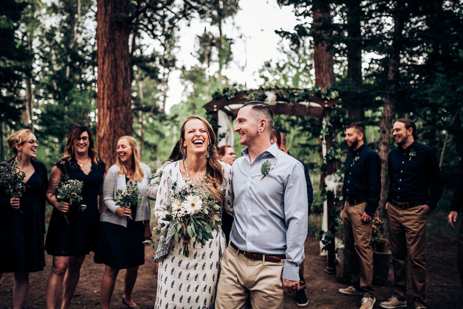 Joyful laughter during an outdoor celebration with pine trees and a wooden arch.