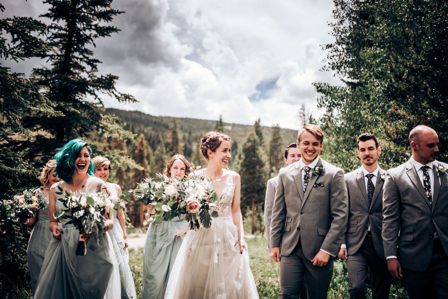 A wedding party in grey attire poses together against a mountainous forest backdrop.