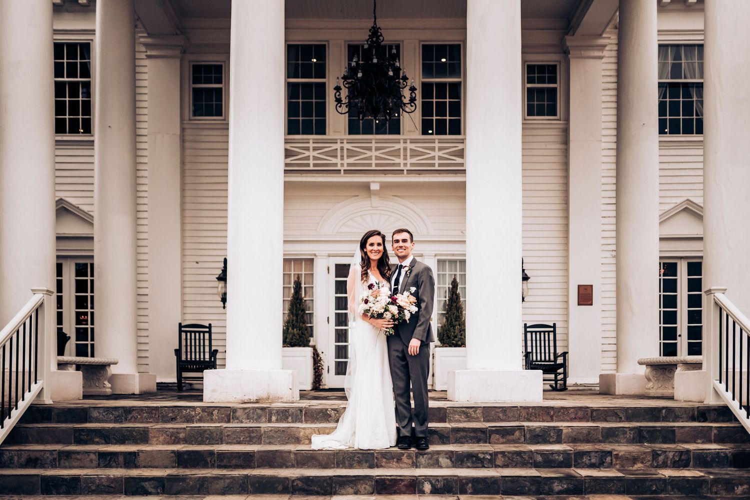 Wedding couple standing on grand white columned mansion steps.