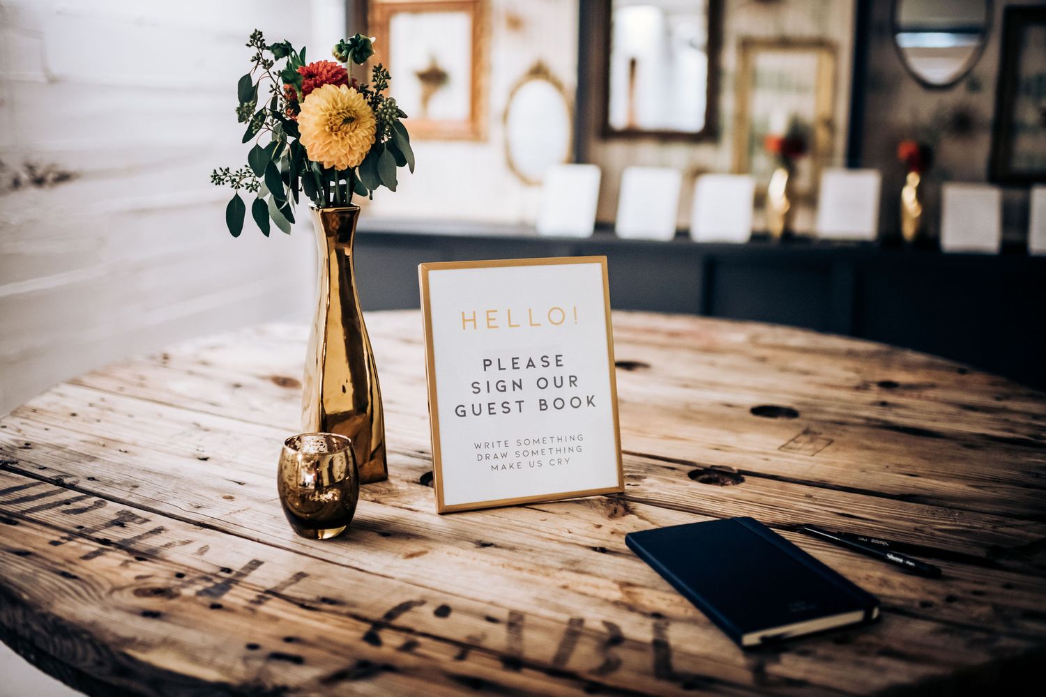 Guest book sign on wooden table with single flower in gold vase.