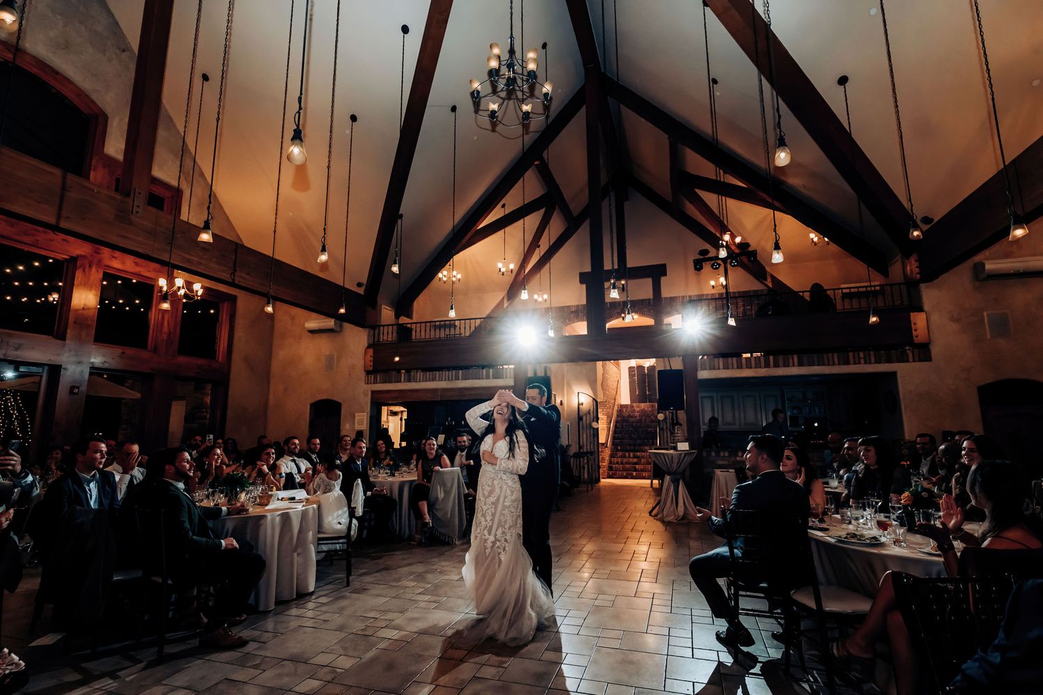 A couple shares their first dance at a rustic wedding reception with exposed wooden beams and romantic lighting.