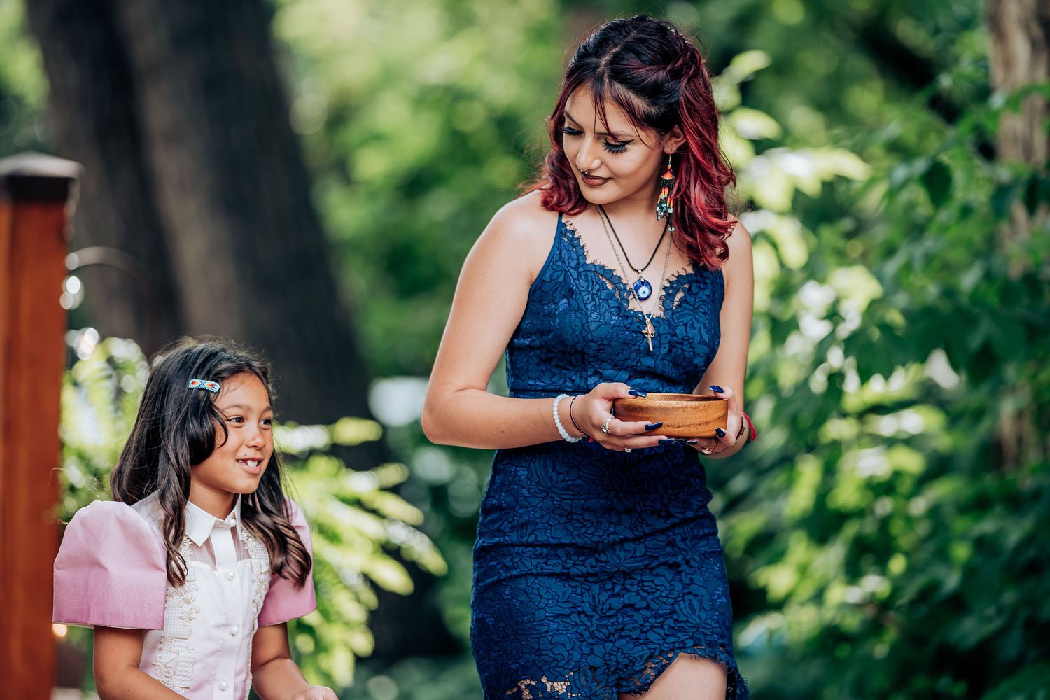 Two attendees in formal attire share a moment while looking at something during an outdoor event.