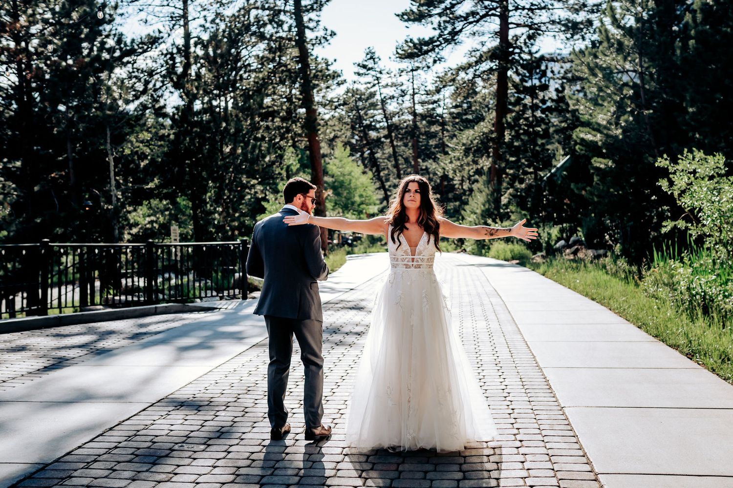 Wedding couple stands on paved pathway surrounded by pine trees at mountain venue.