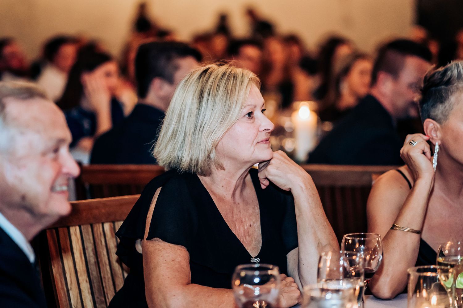 Wedding guests enjoy reception dinner in candlelit industrial venue with brick walls.