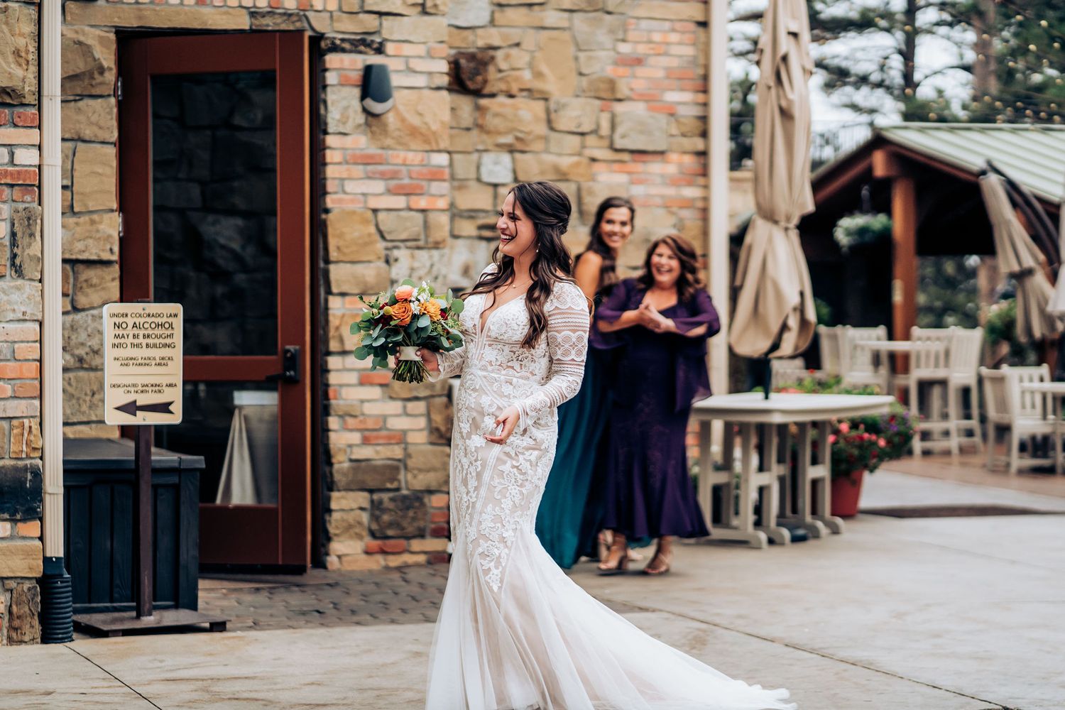 Bride in lace mermaid gown walks outside rustic stone venue with trailing dress.