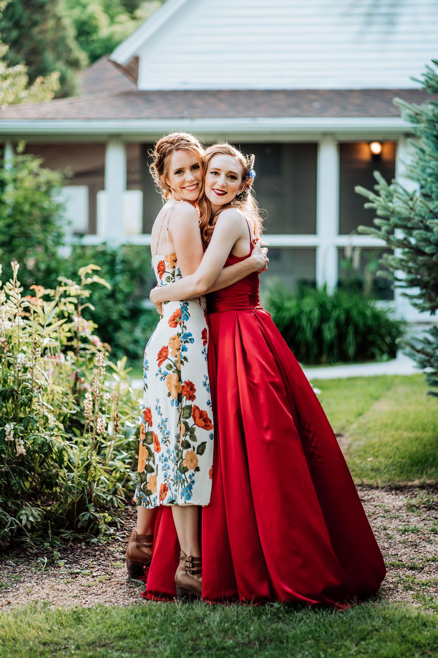 Two people embrace outdoors wearing a red ballgown and floral dress.
