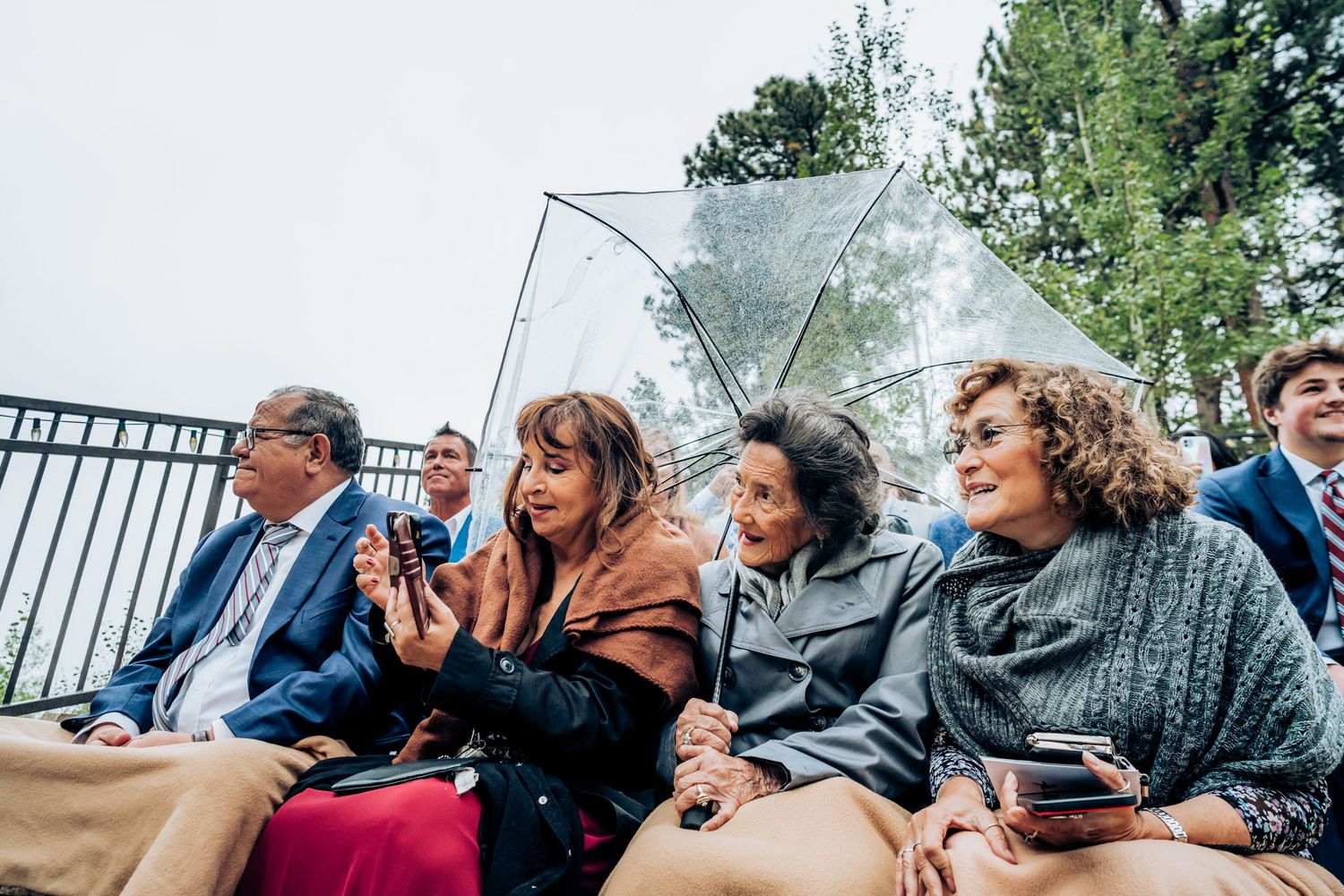 Wedding guests sitting with clear umbrellas during outdoor ceremony.