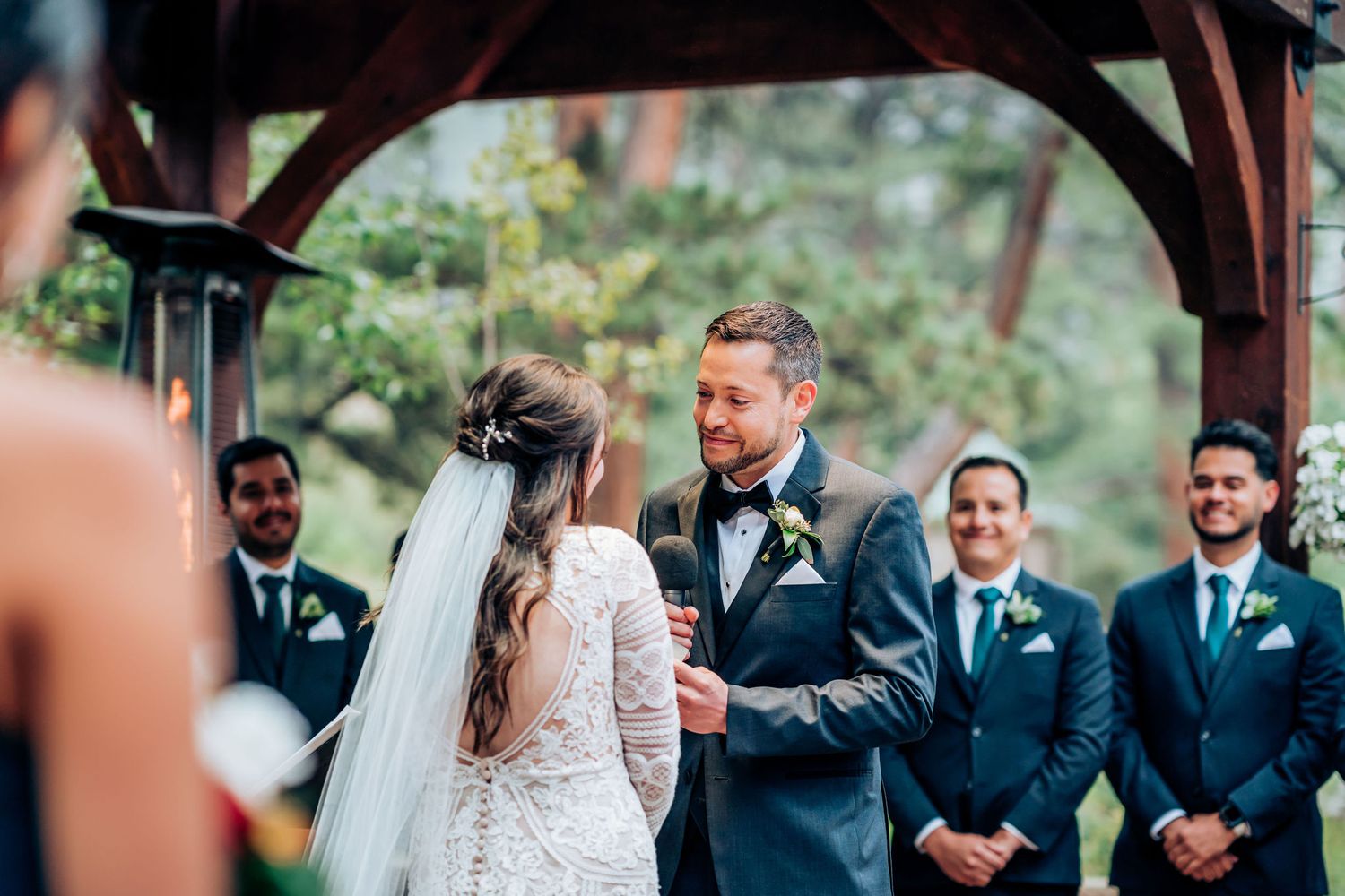 Intimate wedding ceremony moment captured under rustic wooden pergola during vow exchange.