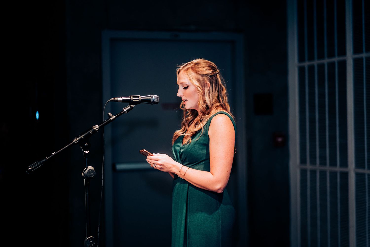 A speaker in an elegant green dress delivers remarks at a microphone stand.