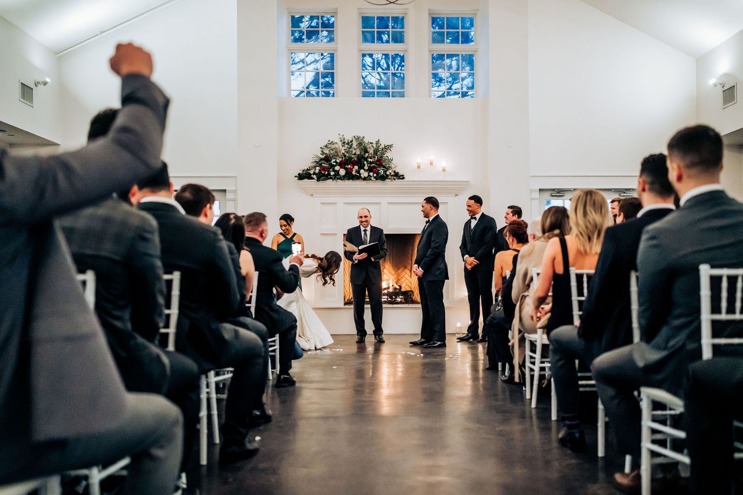 A modern wedding ceremony takes place in a bright white chapel with blue stained glass windows.