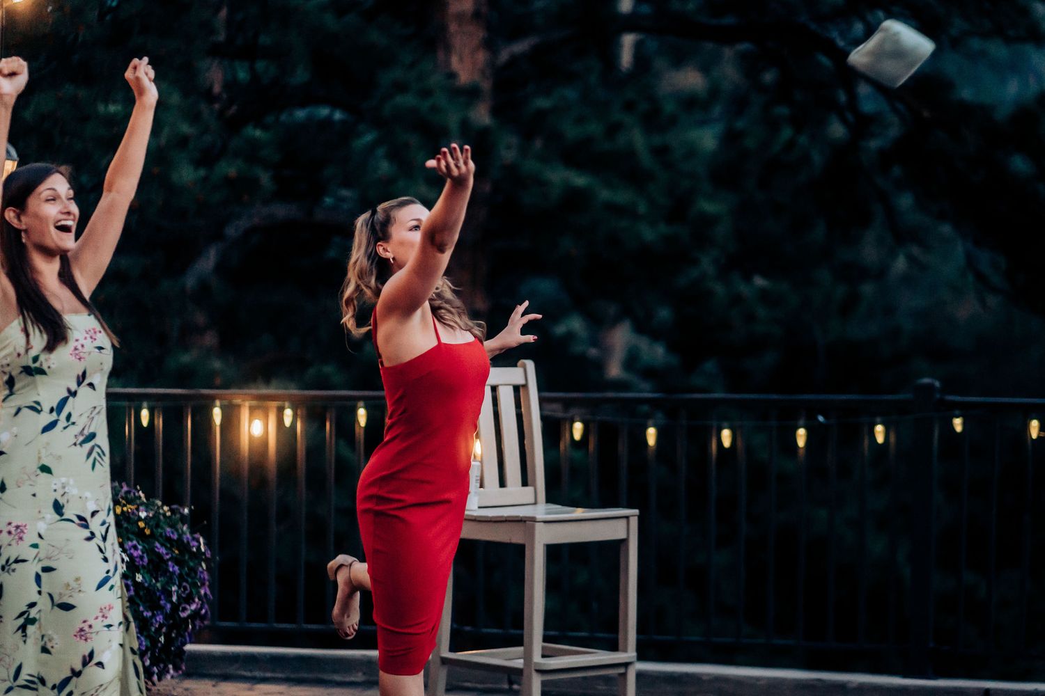 Two women dance enthusiastically outdoors at night with string lights in the background.