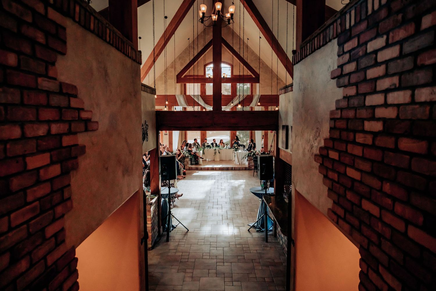 View down a brick-lined hallway towards a wedding reception venue with vaulted ceilings.