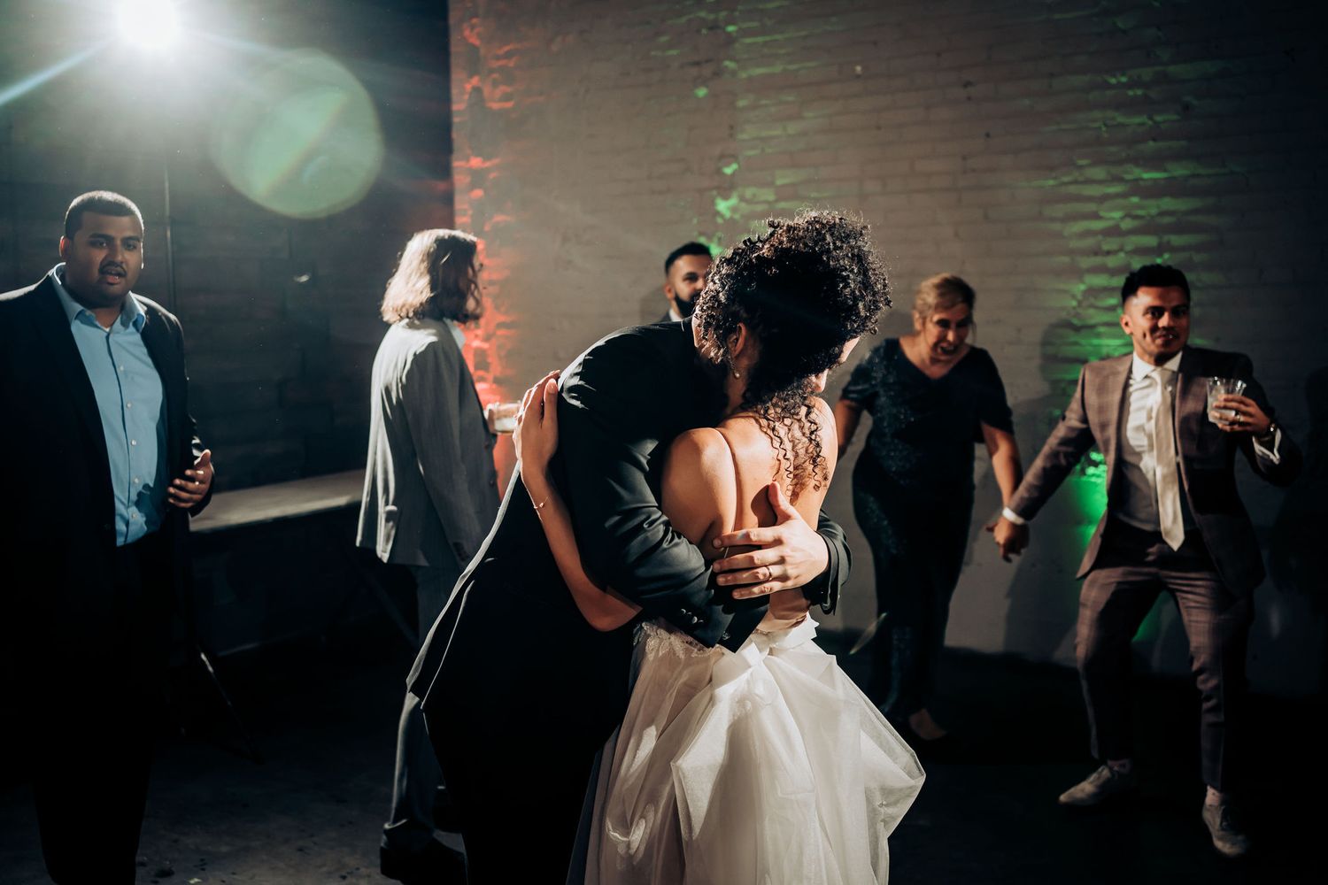 Couple embraces while dancing at wedding reception as guests celebrate around them.