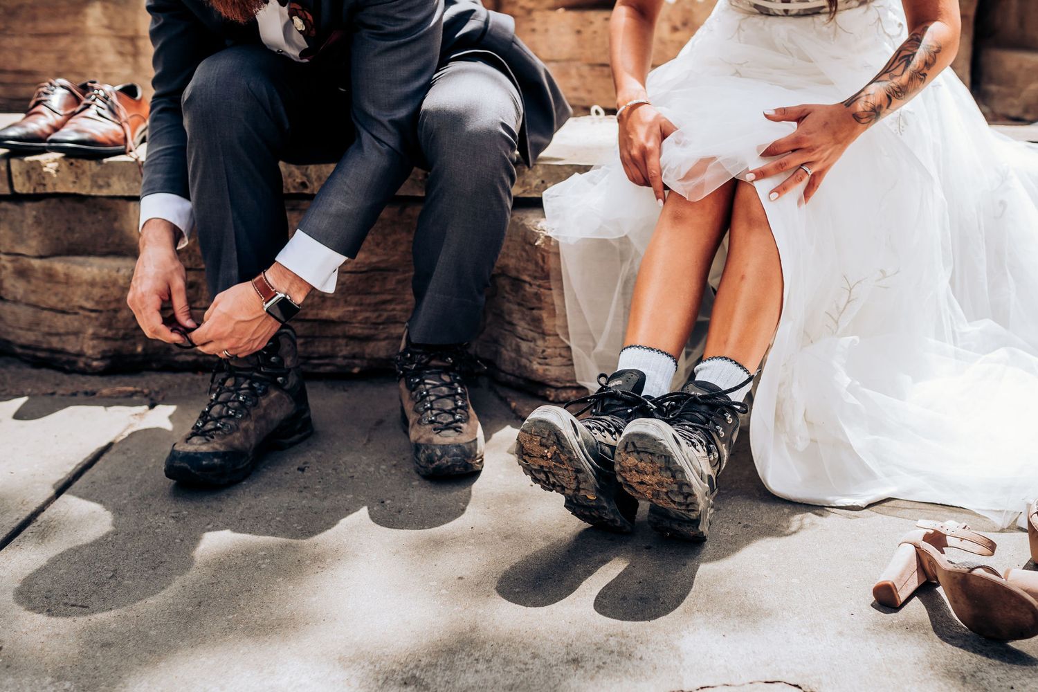 Wedding couple lacing up hiking boots while sitting on wooden steps in formal attire.