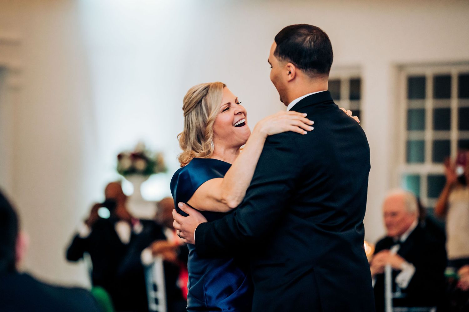 Couple shares romantic dance moment in elegant venue with white decor and ambient lighting.