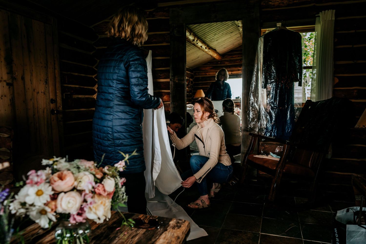 Wedding preparations in a rustic log cabin with hanging dress and floral arrangements.