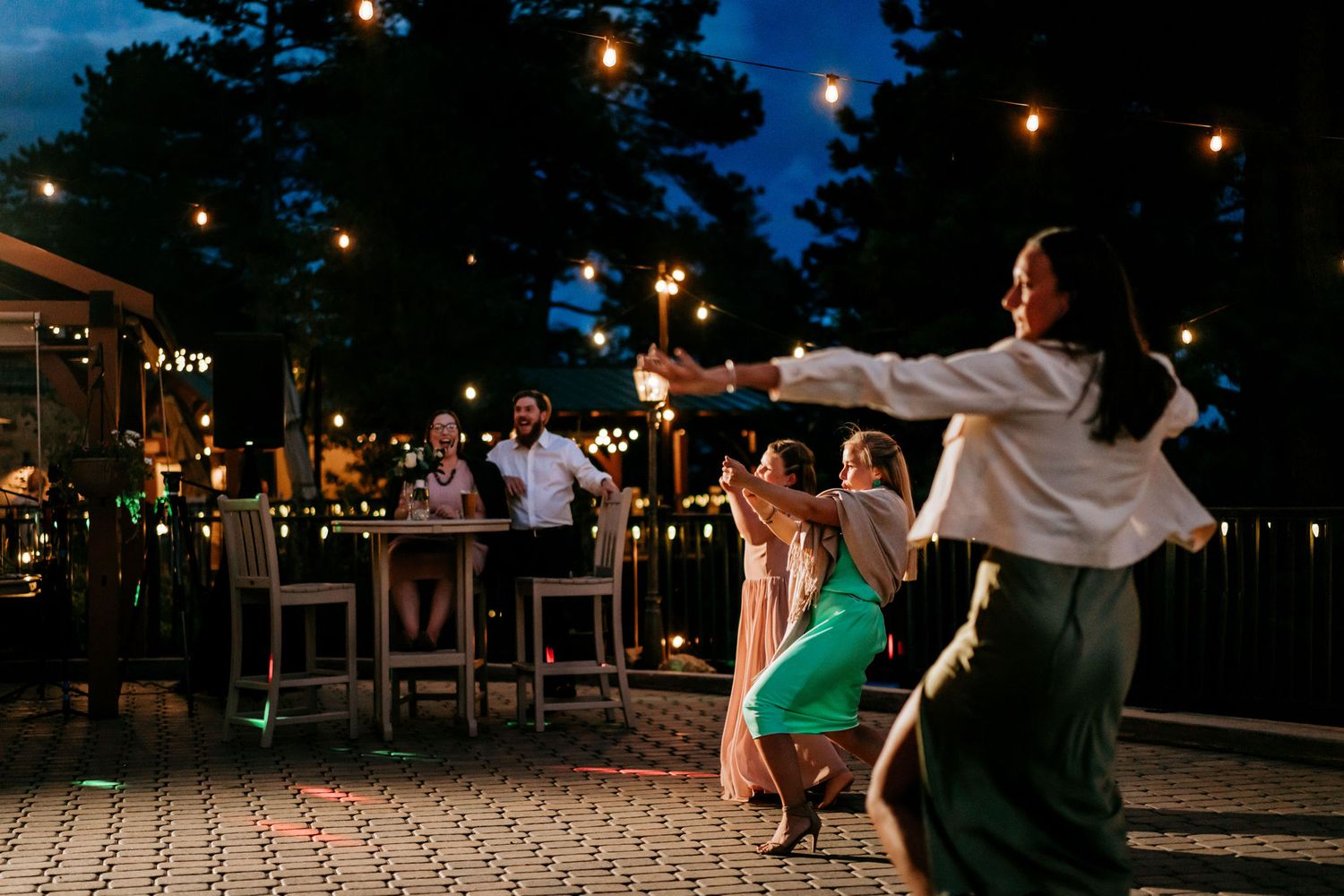 Lively dance floor scene at outdoor wedding reception with string lights overhead.