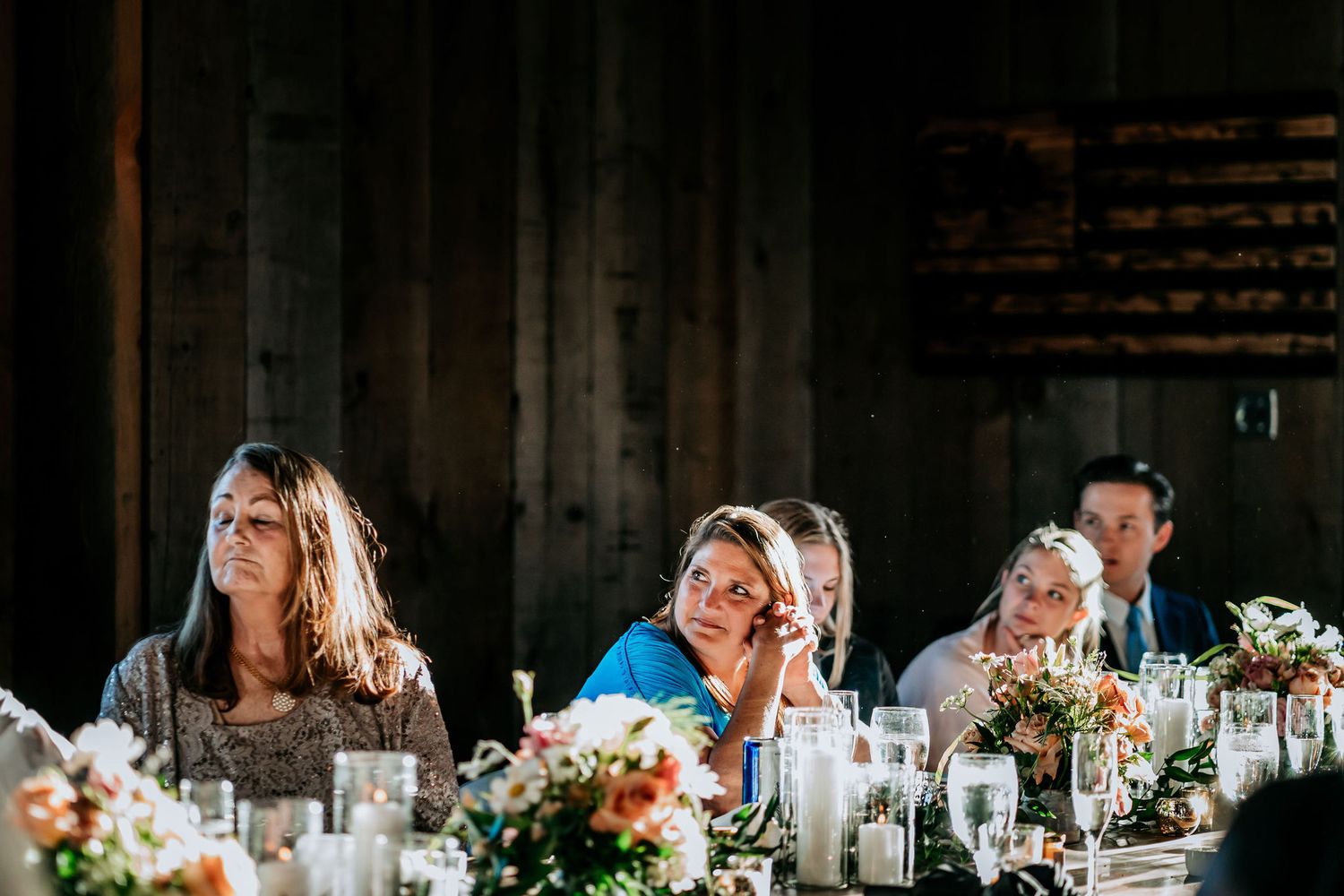 Guests react emotionally to speeches during an elegant dinner reception with floral table decorations.