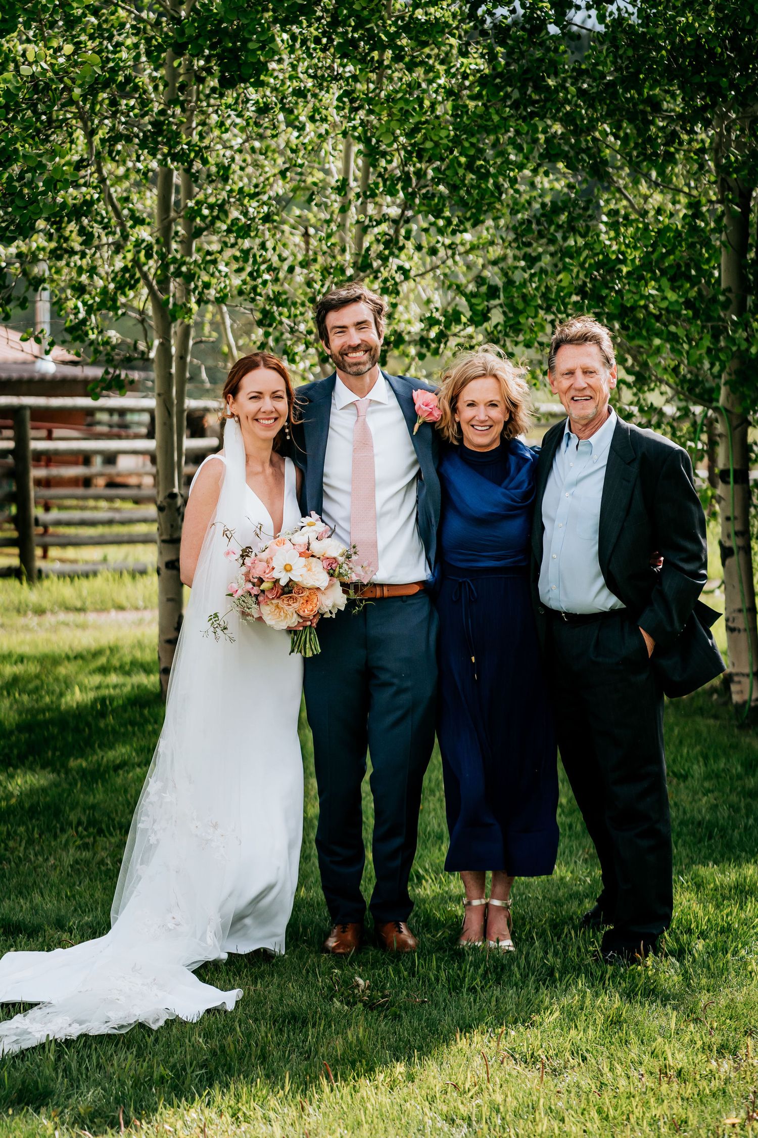 Wedding couple poses with family members outdoors against a backdrop of green trees.