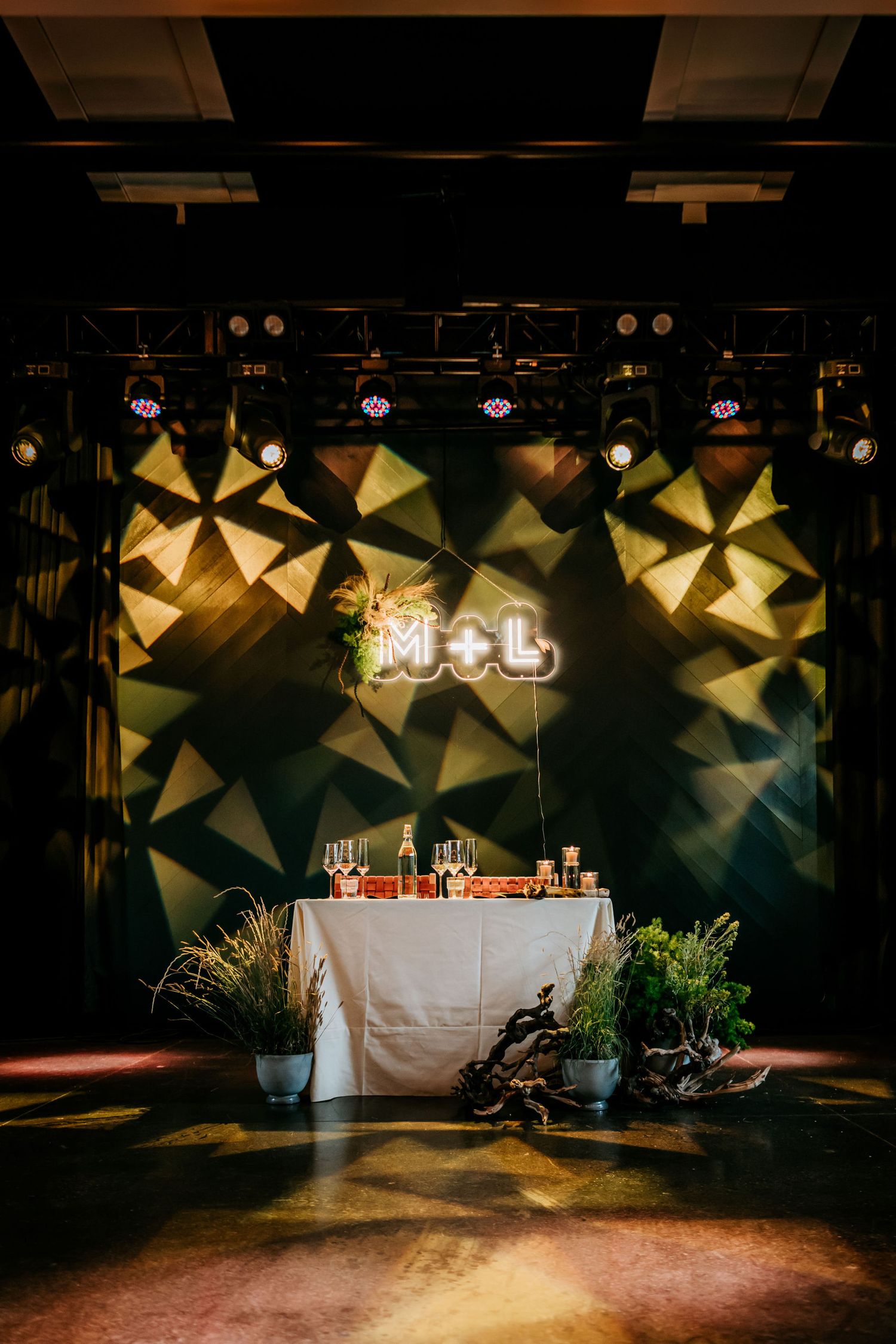 Illuminated M+L sign with geometric backdrop and decorated table at an event venue.