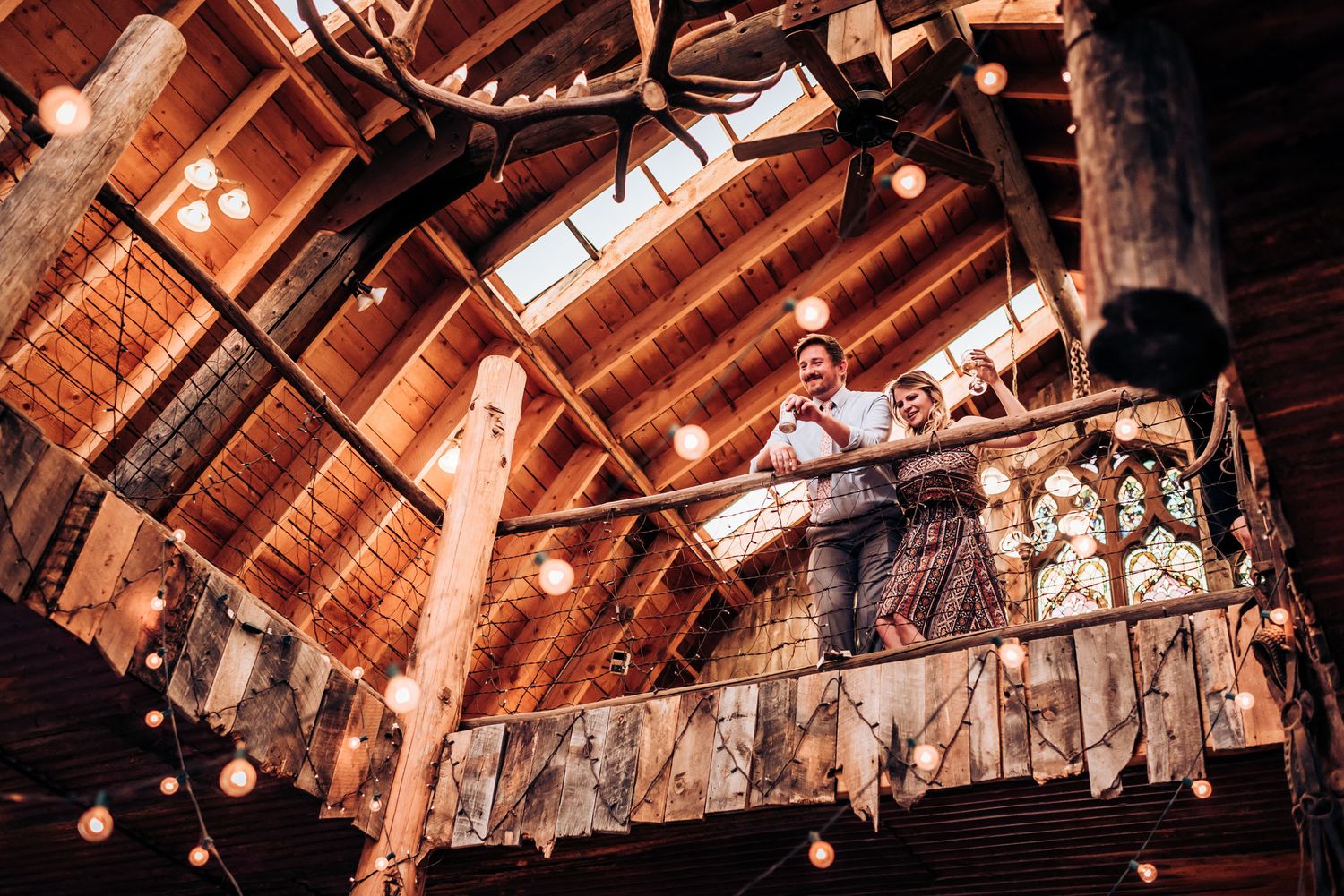 Rustic barn wedding venue interior with exposed wooden beams and hanging string lights creating warm ambiance.