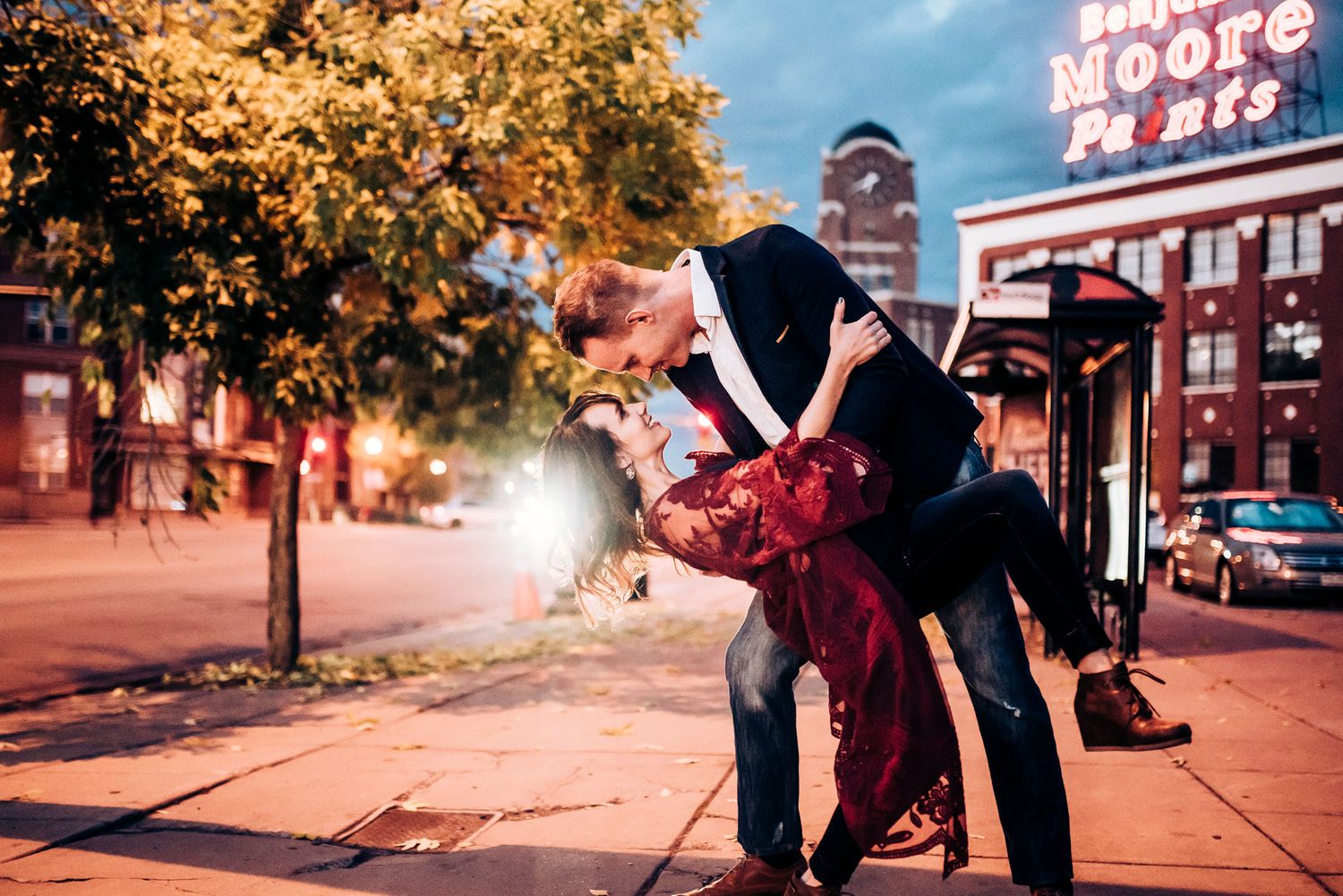 A romantic dip pose on a city street at night with neon lights in the background.