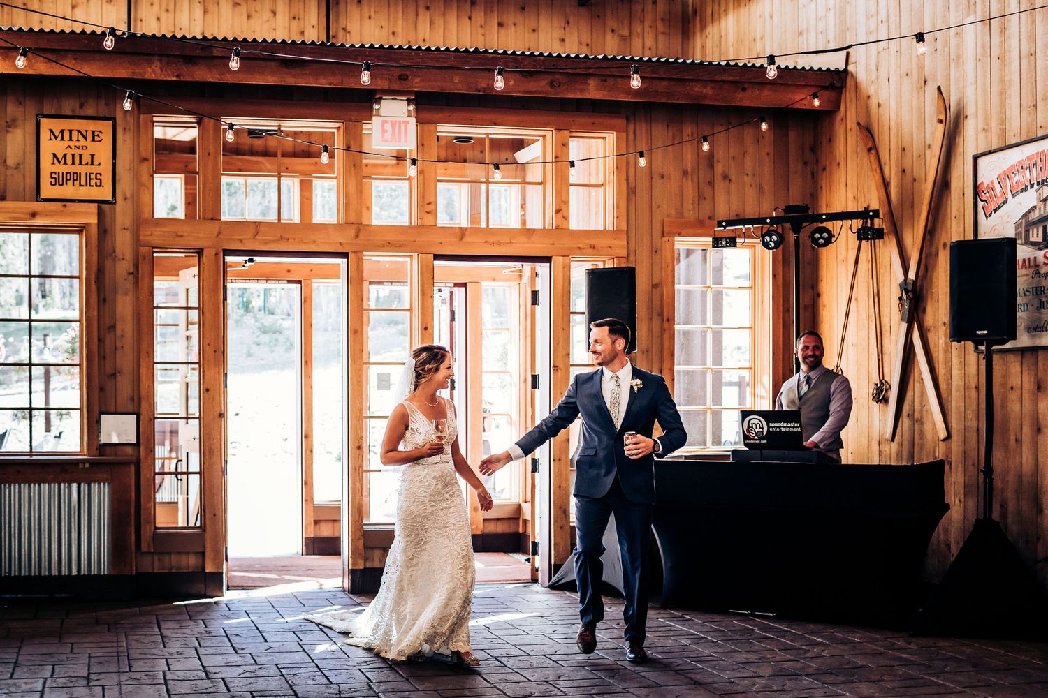 Dancing couple in formal attire inside a rustic wooden reception venue.