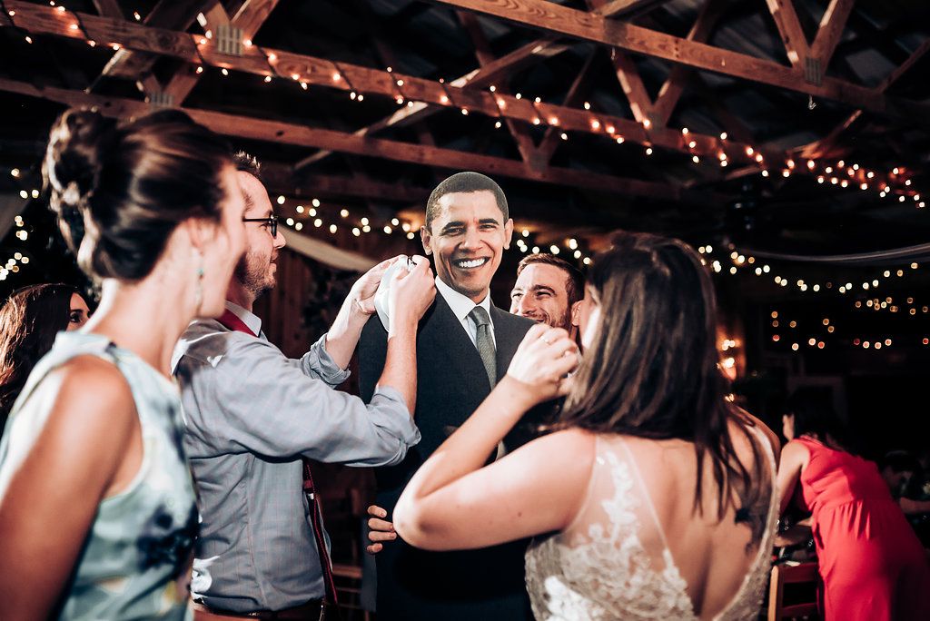 Wedding guests enjoy themselves on the dance floor under rustic wooden beams with string lights.