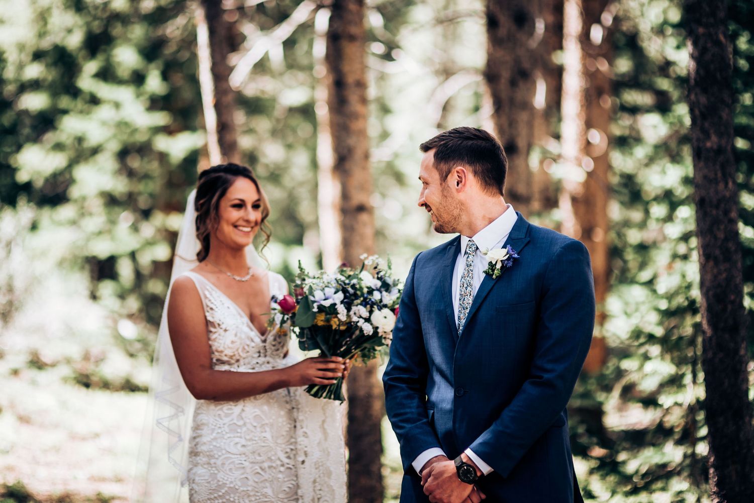 A couple shares an intimate moment during their forest wedding ceremony while holding a colorful bouquet.