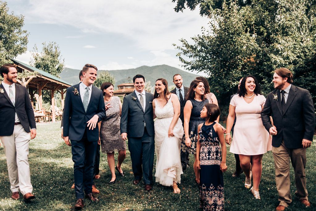 Wedding party gathered outdoors with mountains and greenery in the background.