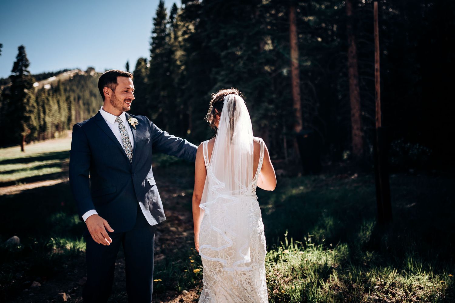 A wedding couple shares a moment on a mountainside with evergreen trees in the background.
