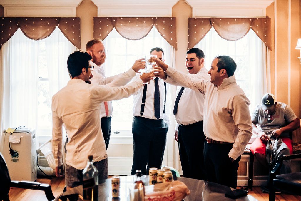 A group of groomsmen sharing drinks and toasting together in formal attire.