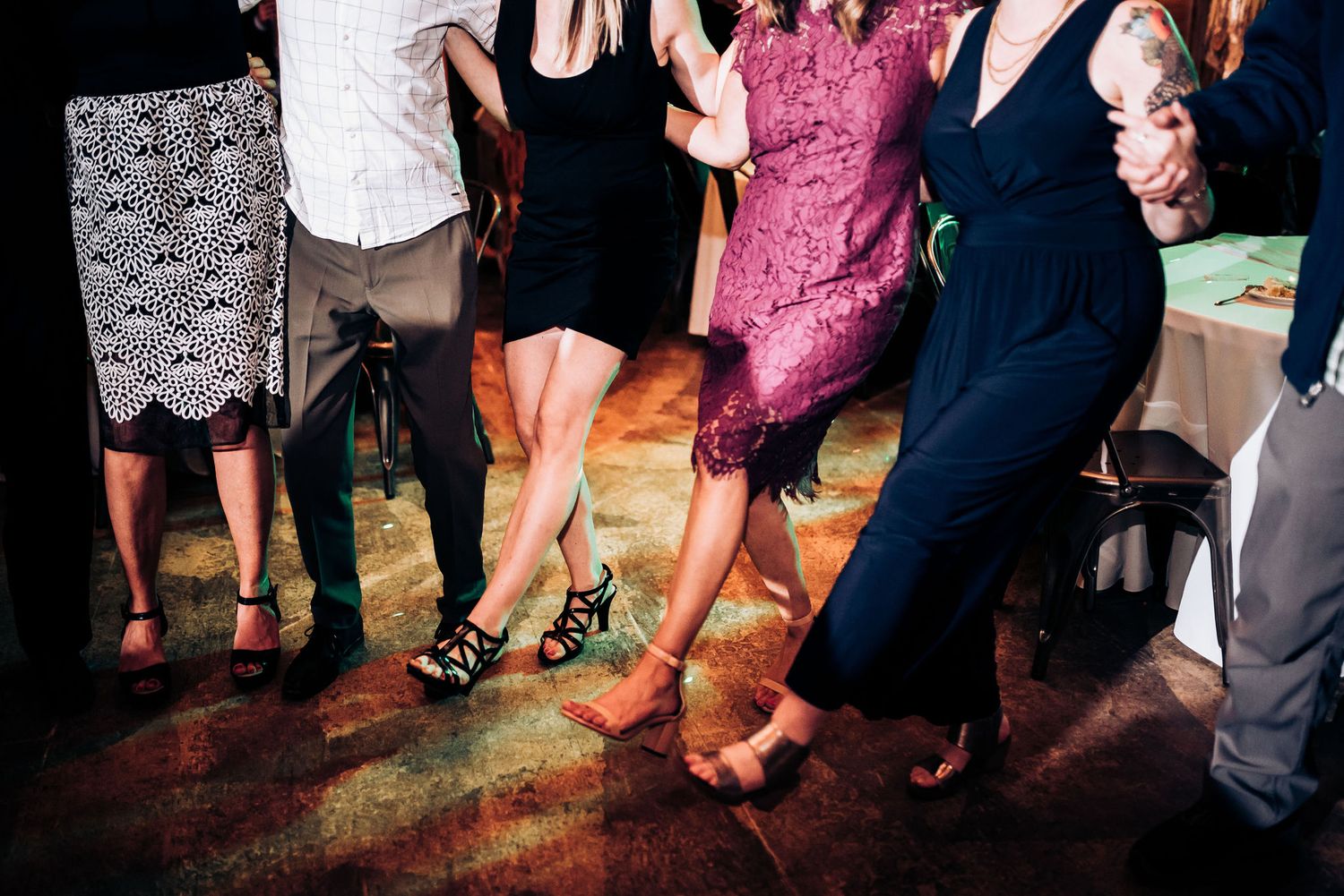 Dancing feet and flowing dresses move across a darkened dance floor at a wedding celebration.