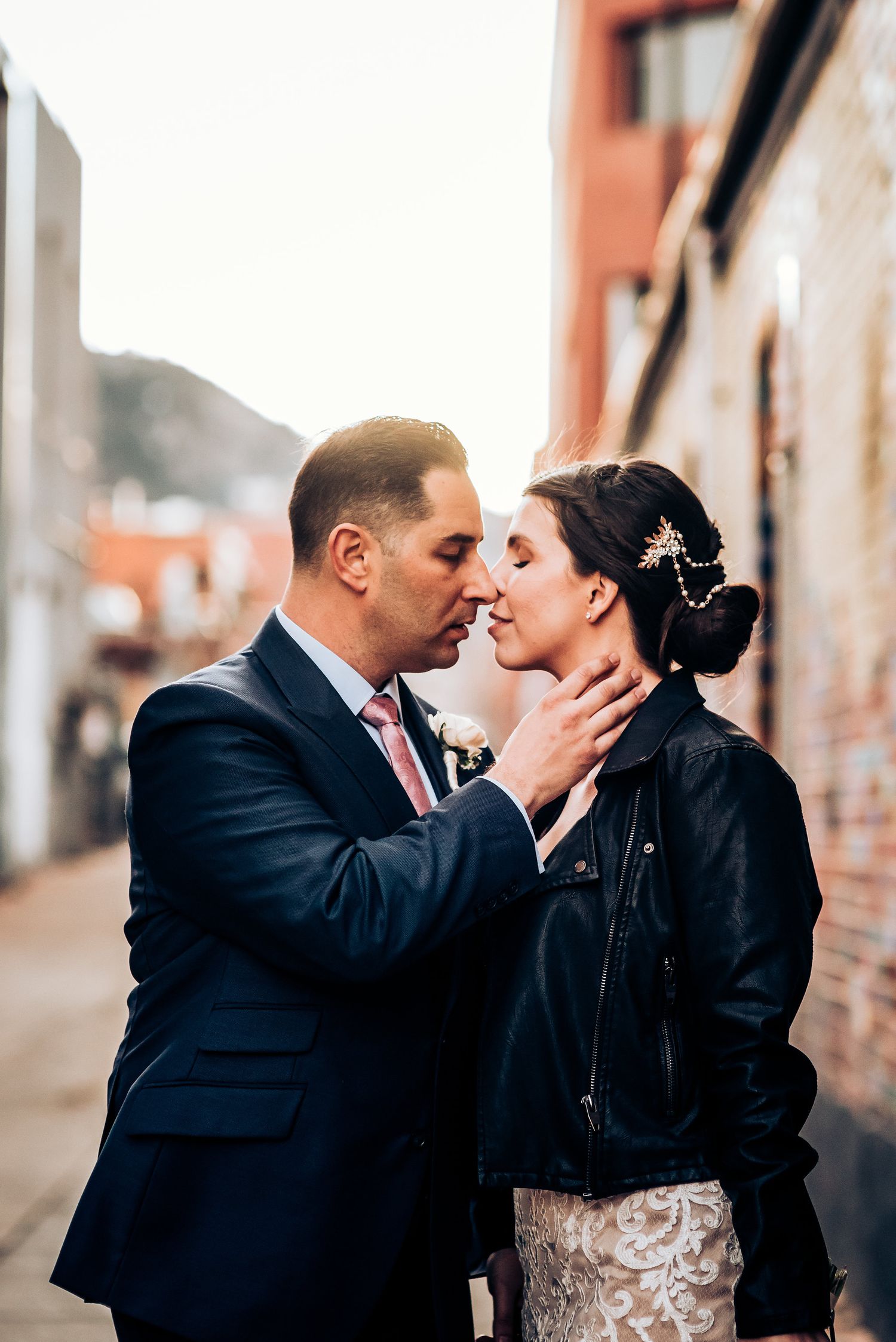 Tender moment between newlyweds against brick wall in urban setting.