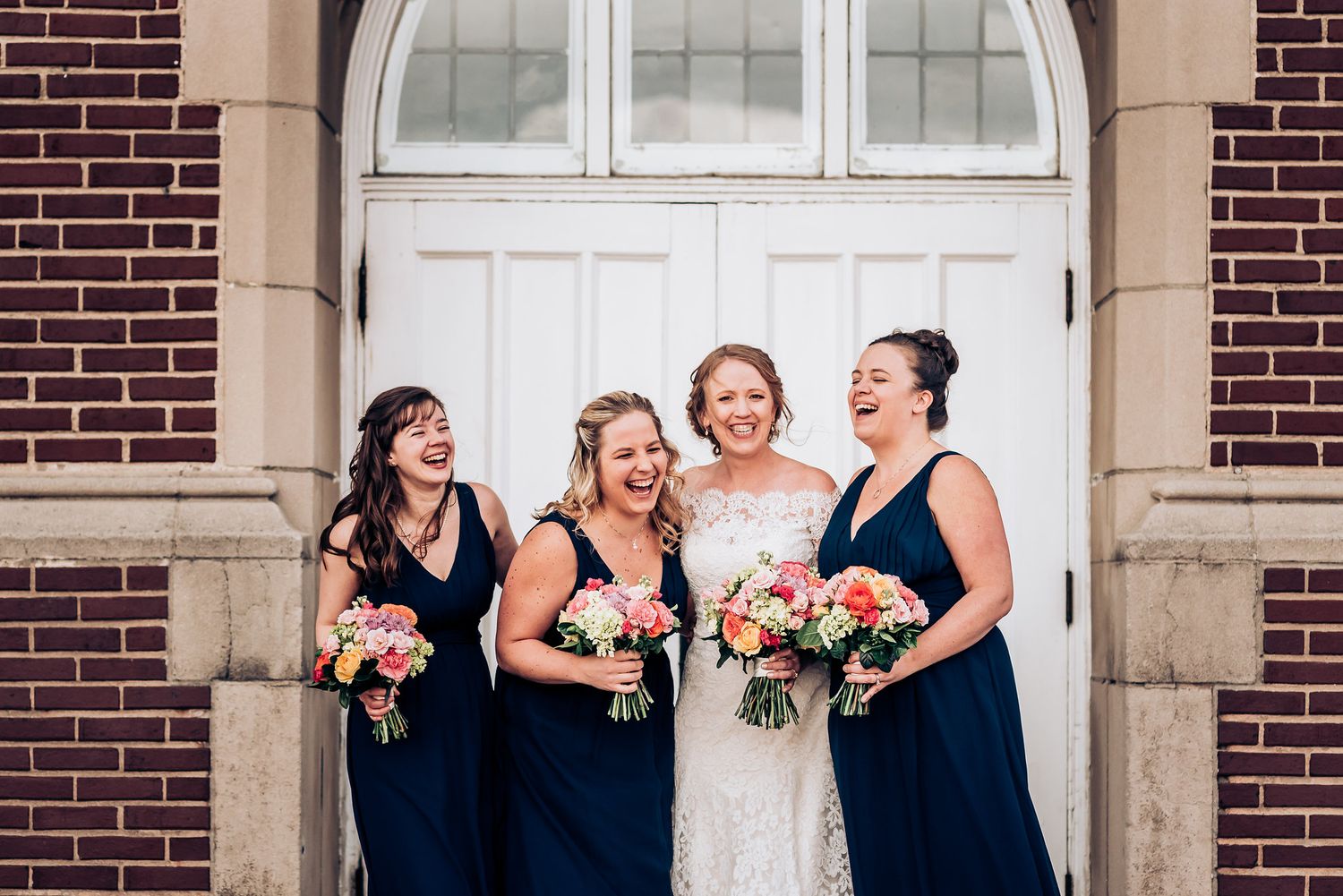 Cheerful wedding party in navy dresses share laughter in front of classic church architecture.