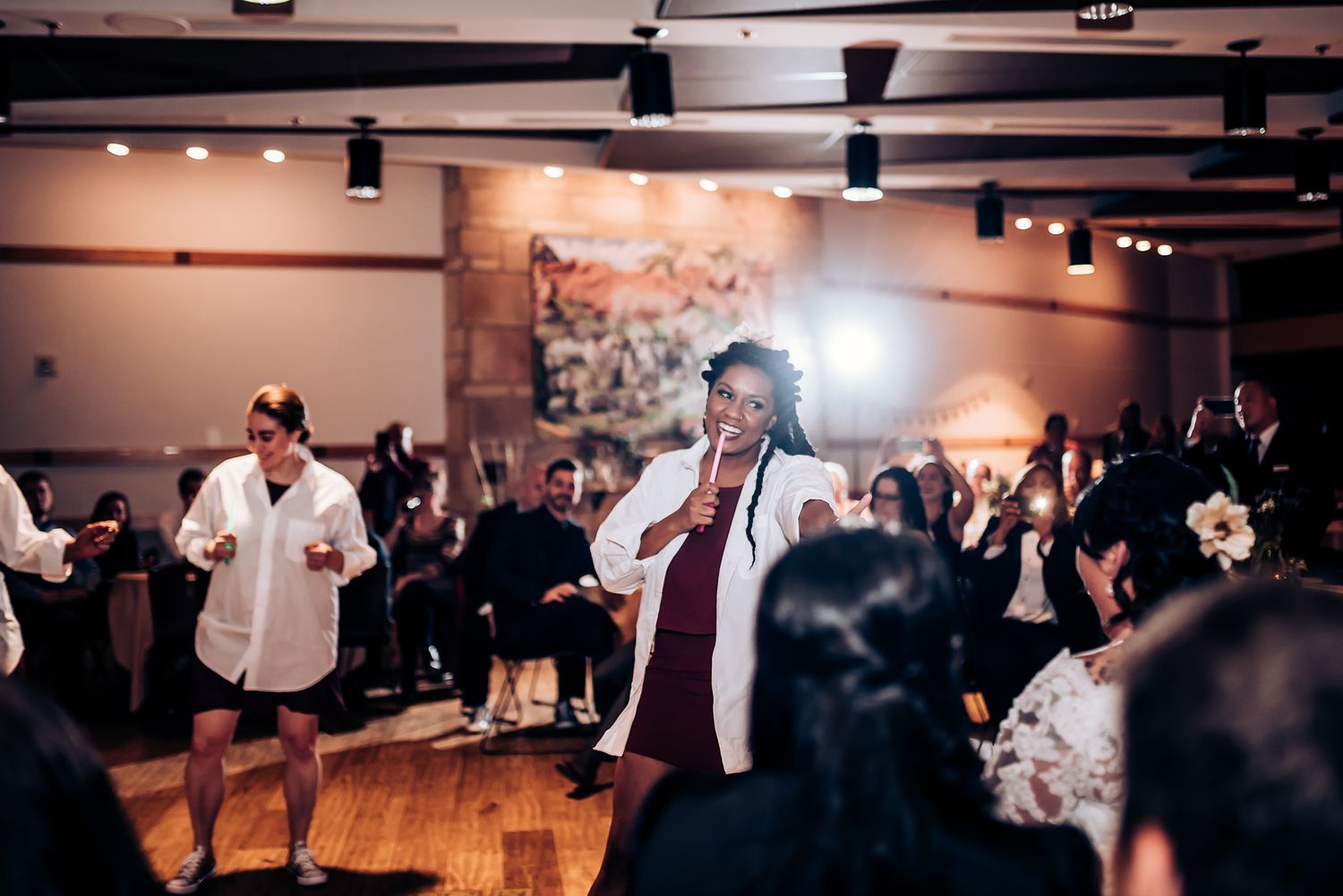 People dancing and celebrating at an indoor wedding reception with mood lighting and hardwood floors.